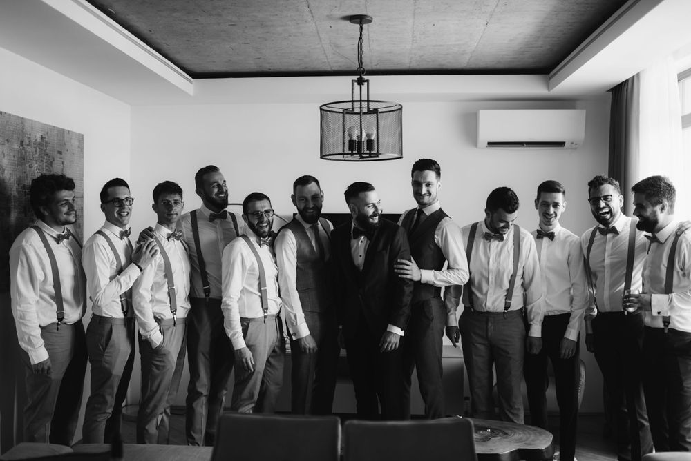 Large wedding party group photo with groomsmen in white shirts and suspenders.