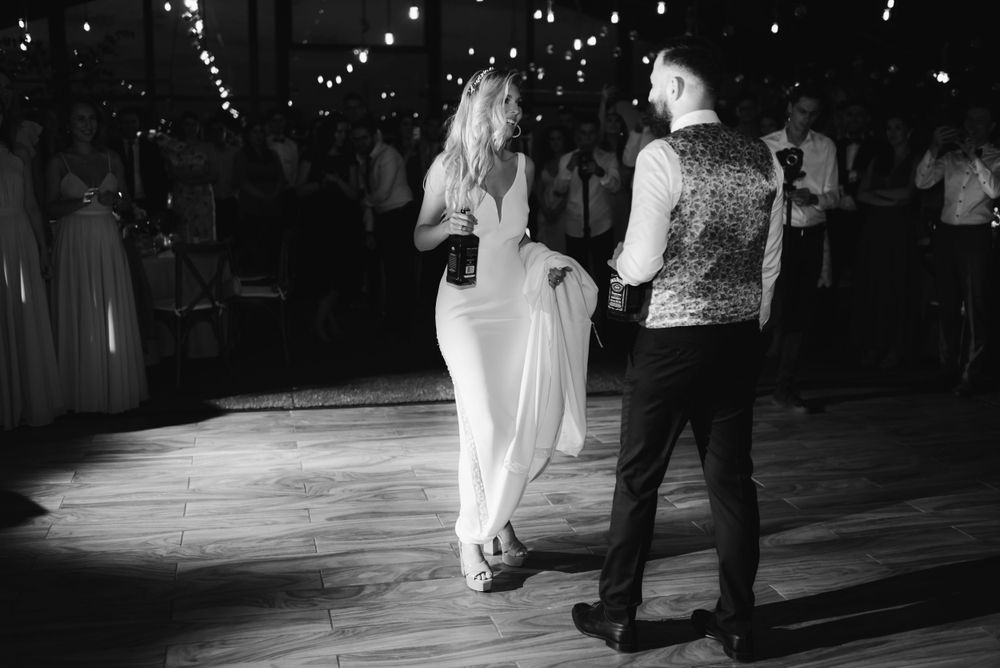 Black and white photo of a couple dancing at a wedding reception under string lights.