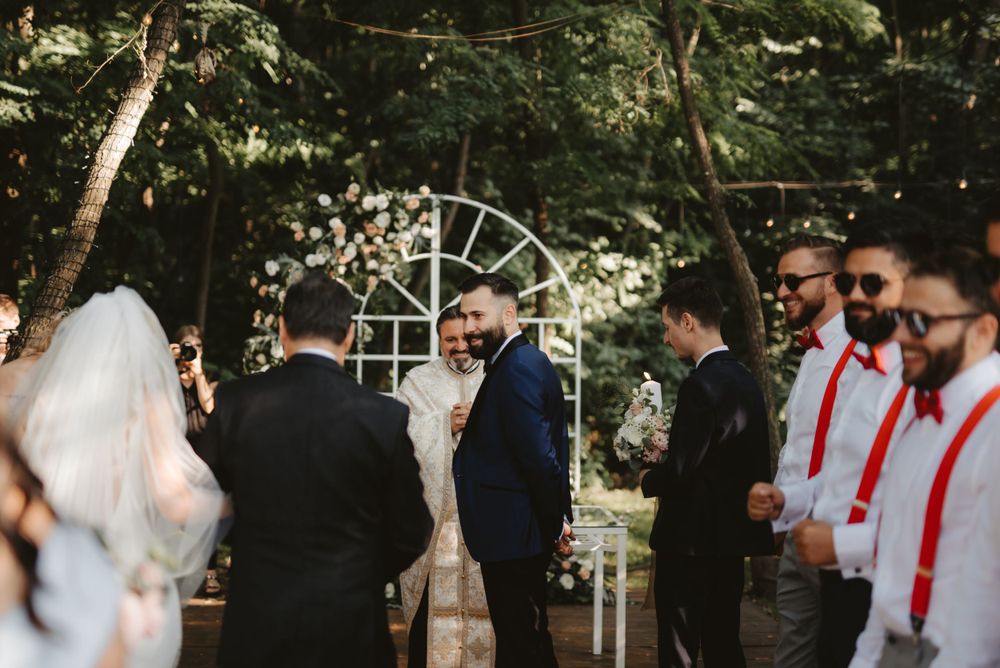 Outdoor wedding ceremony setup with white arch and guests in formal attire.