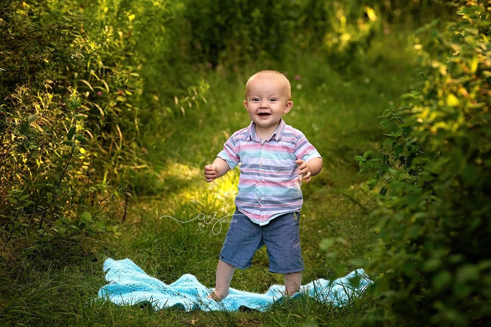 Joyful child in summer clothes stands on blue blanket amid green garden scenery.