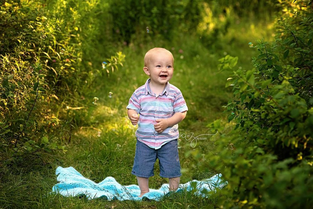 Happy child in casual wear stands on blue blanket along green garden path.