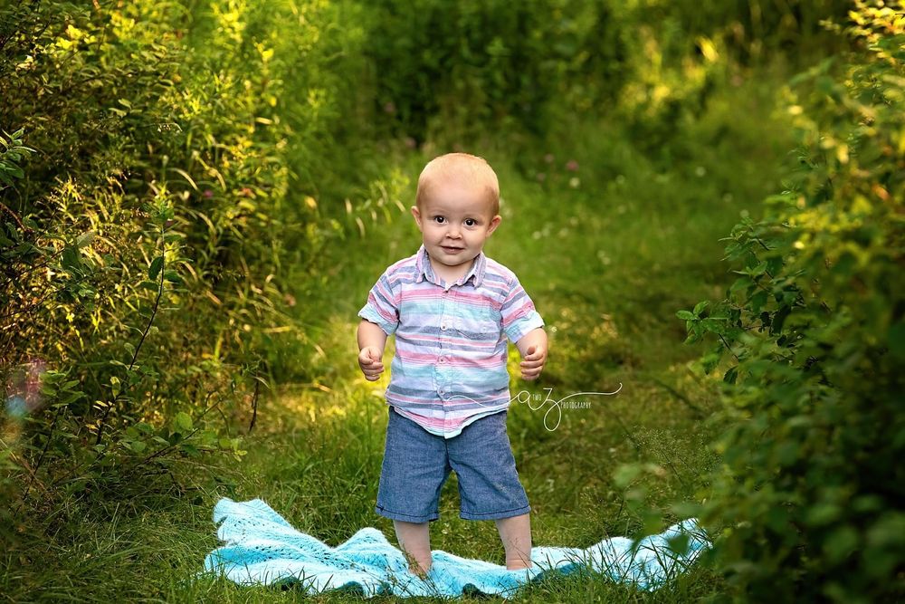 Small child in casual clothes stands on light blue fabric in sunny garden path.