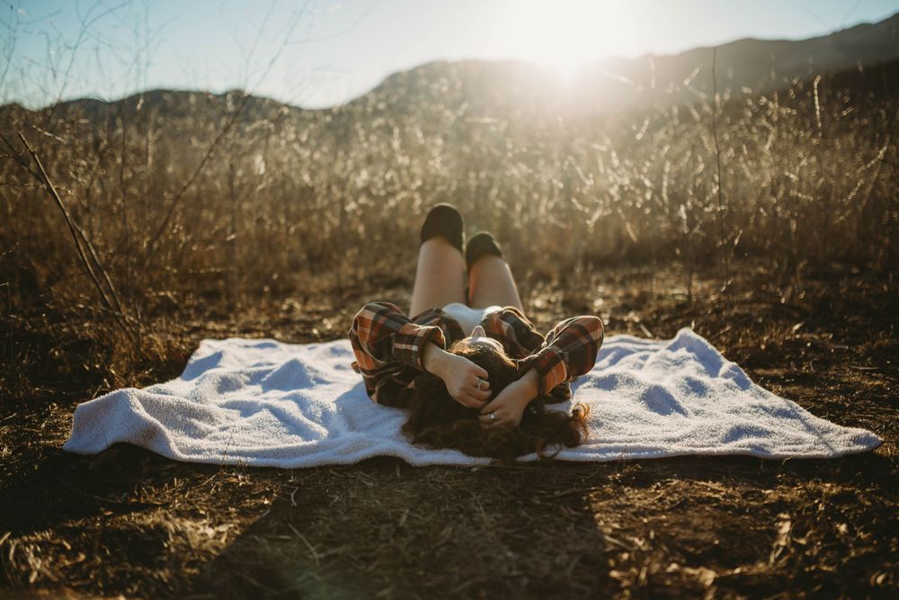 Boudoir model basking in the sunshine in a field of heart grass with mountains at the horizon