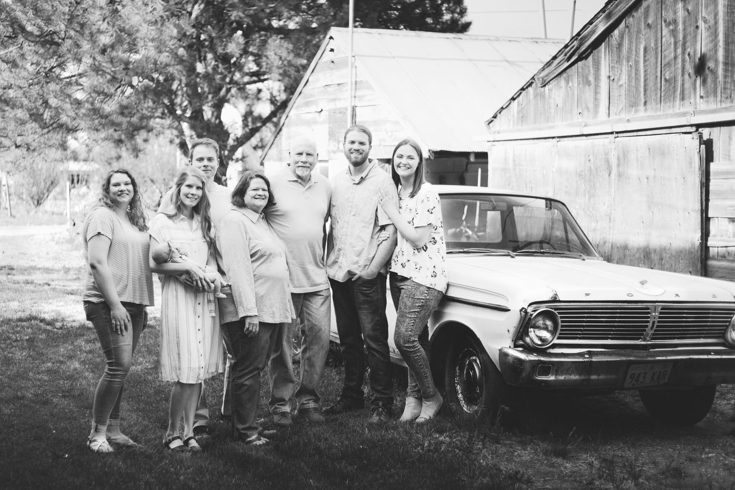 family with grandparents and children posing in front of an old ford and rustic barn