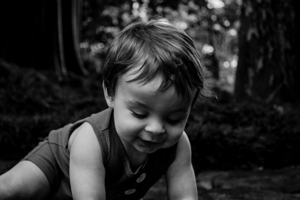 Black and white portrait of playful child exploring outdoors in a forest setting.