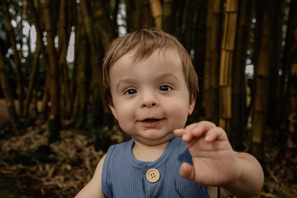 Child in blue overalls smiling while exploring bamboo forest with natural lighting.