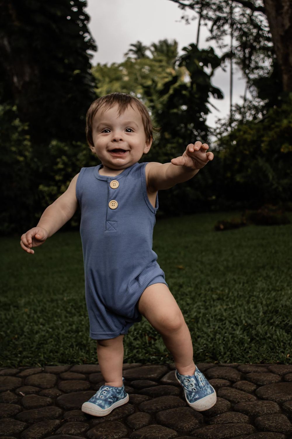 Small child in blue romper and sneakers standing on stone path while playing outside.