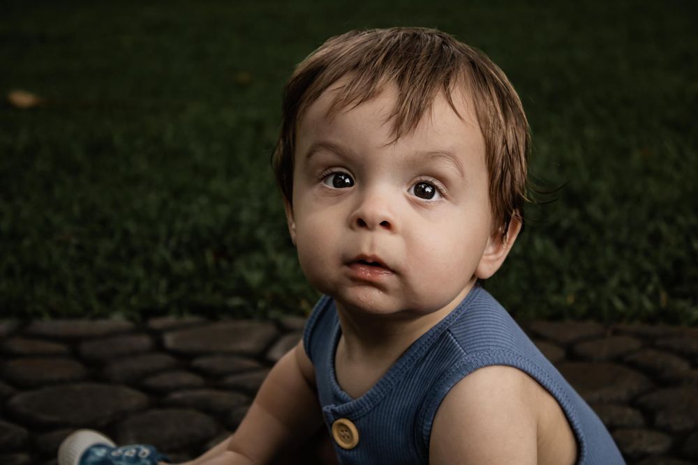 Close up portrait of toddler in blue sleeveless outfit sitting on stone surface.