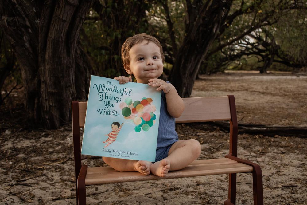 Small child sits on bench holding colorful children's picture book outdoors.
