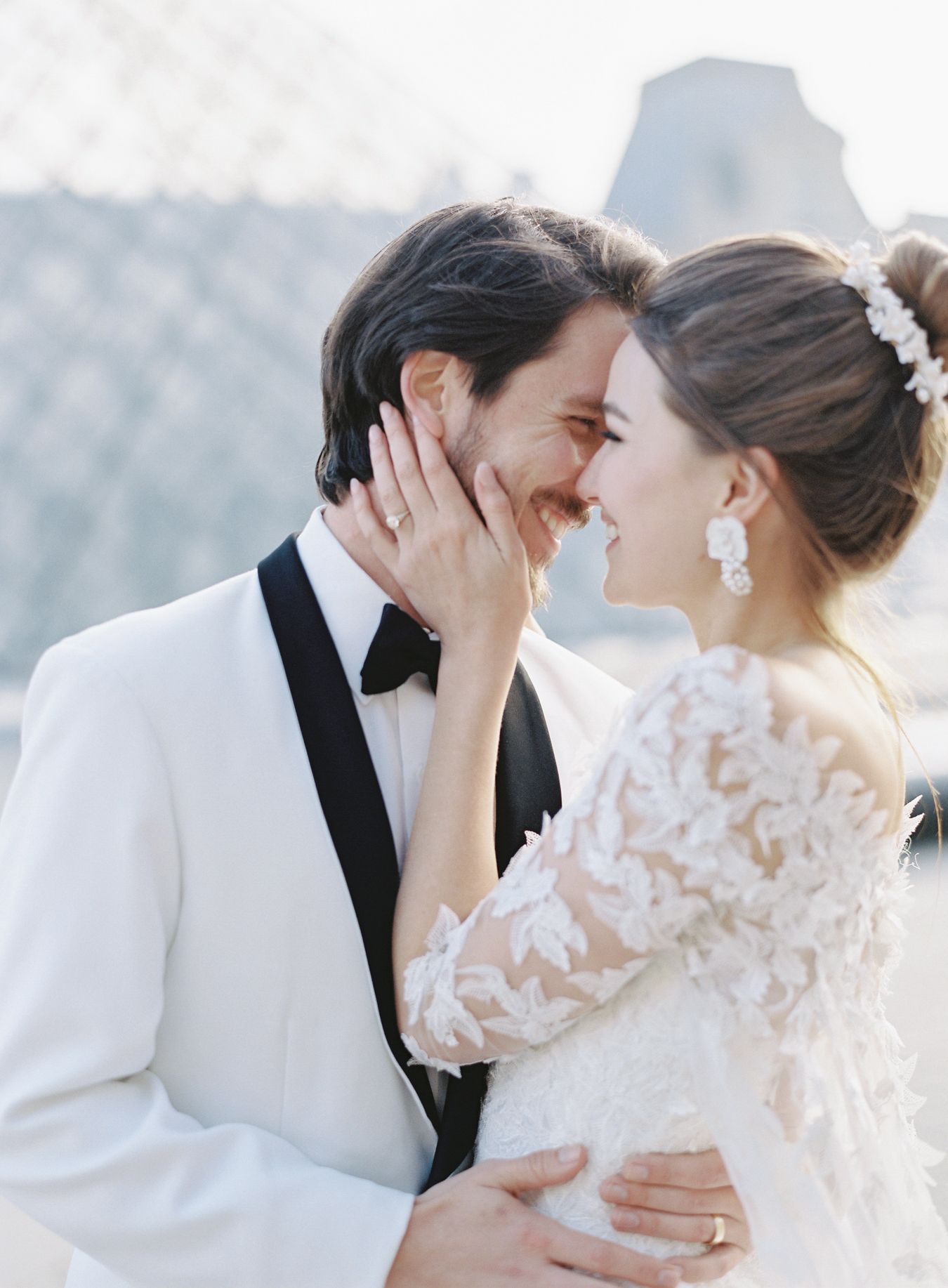 A tender wedding moment captured against the geometric backdrop of the Louvre Museum.