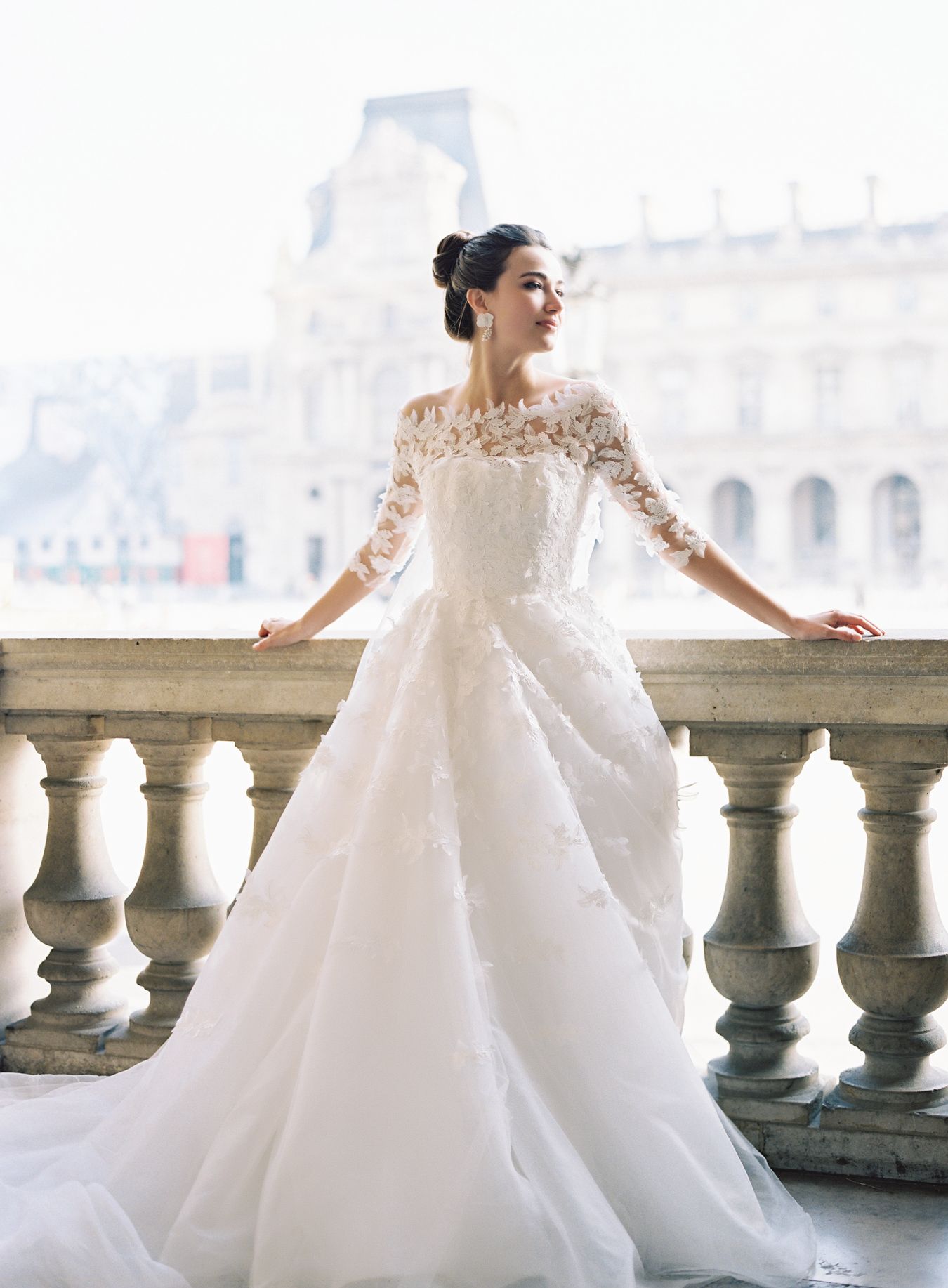 A bride in a lace-sleeve ballgown poses elegantly at the Louvre Palace.