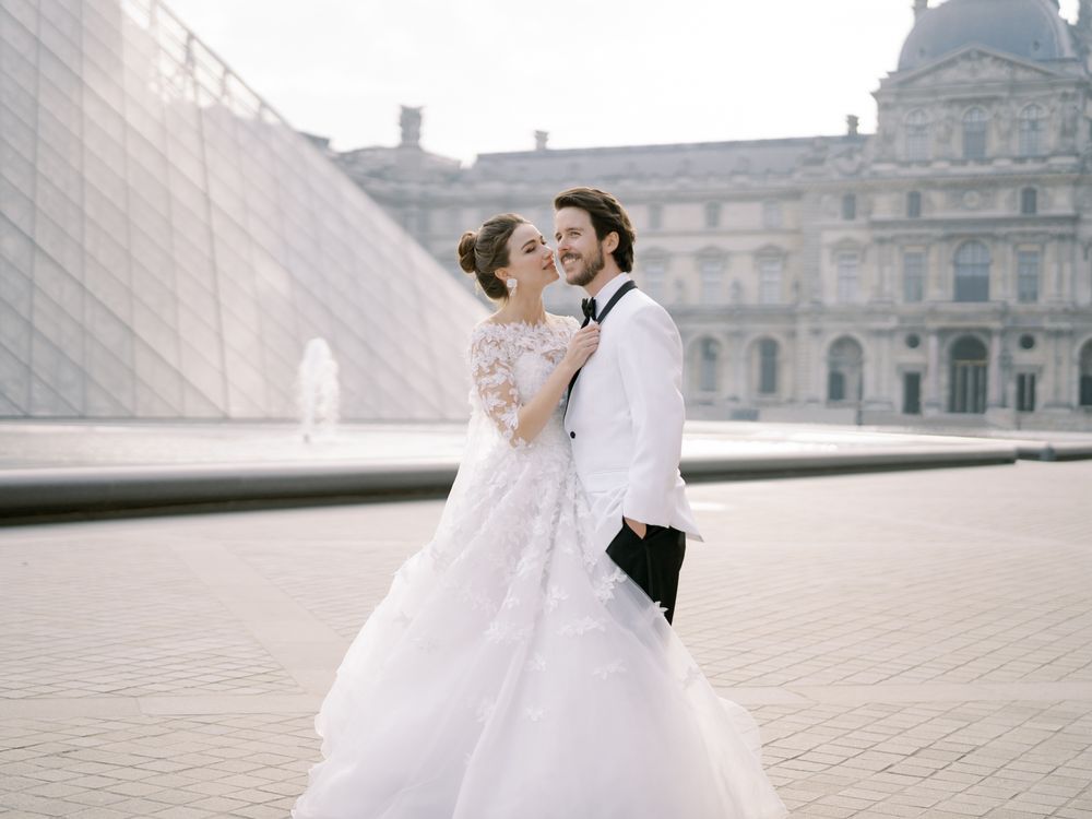 A romantic wedding portrait in front of the Louvre pyramid on a misty day.