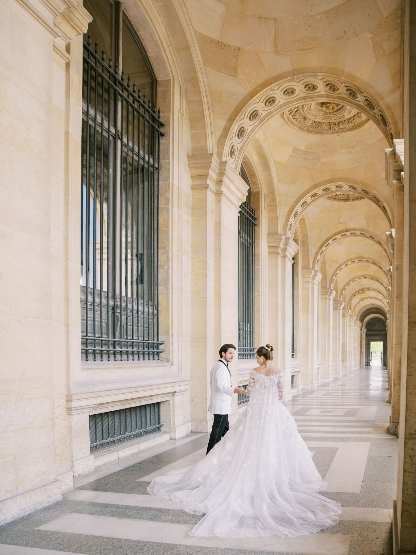 A wedding couple poses in a grand colonnade corridor at the Louvre.