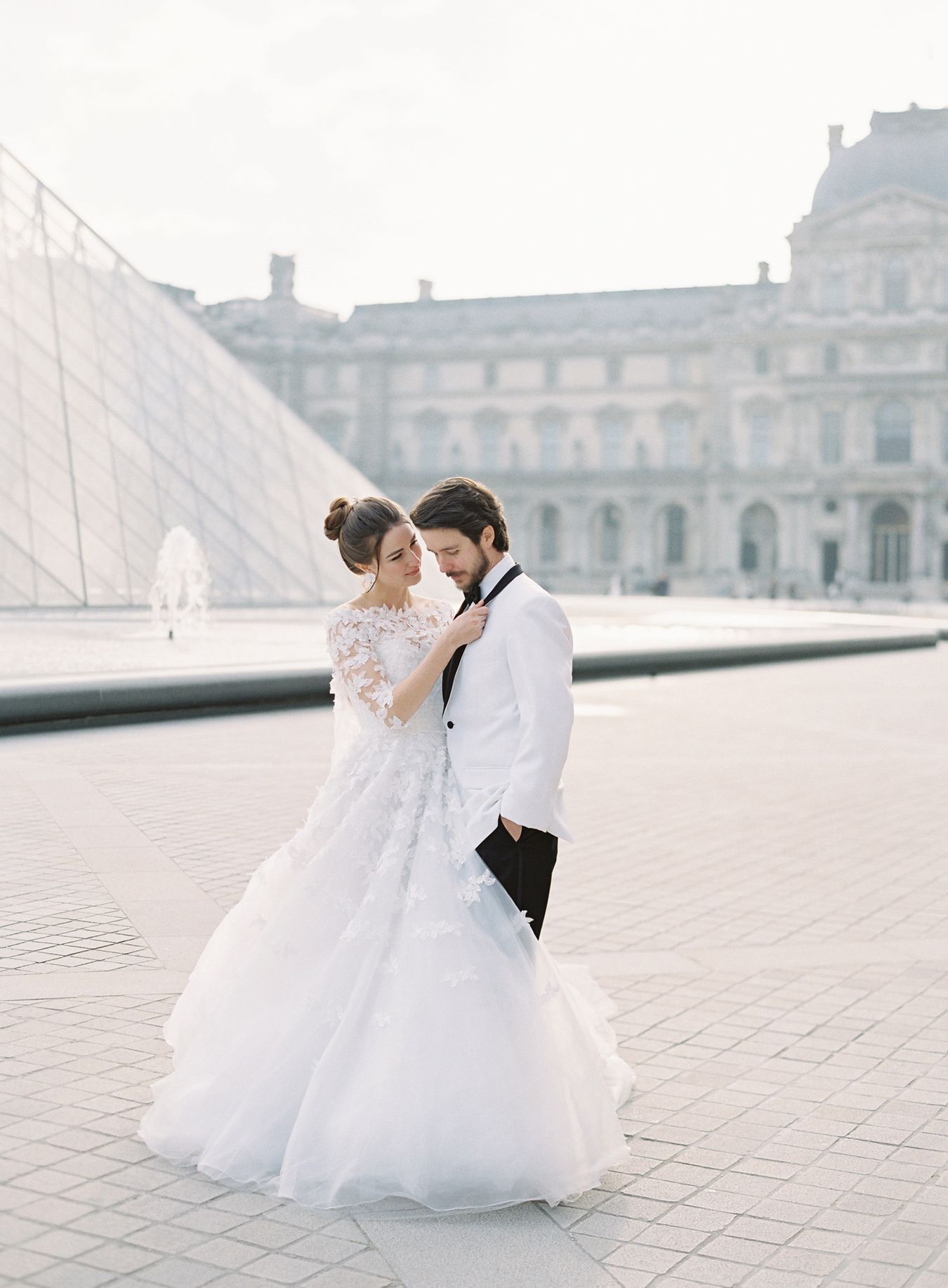 An elegant couple sharing an intimate moment by the iconic glass pyramid at the Louvre.