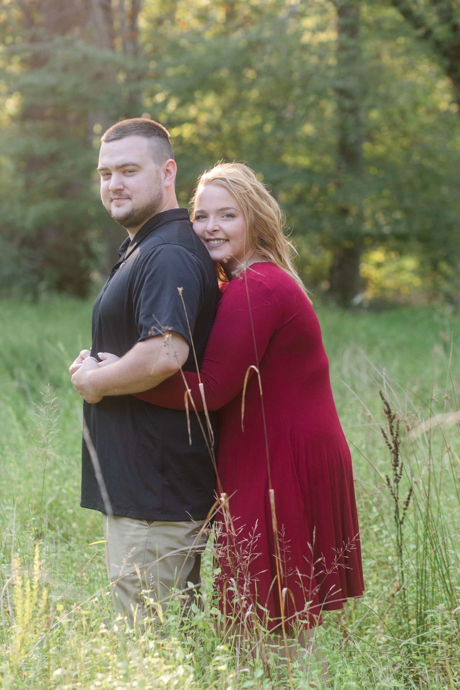 Couple sitting together in tall grass during a golden hour engagement photoshoot.