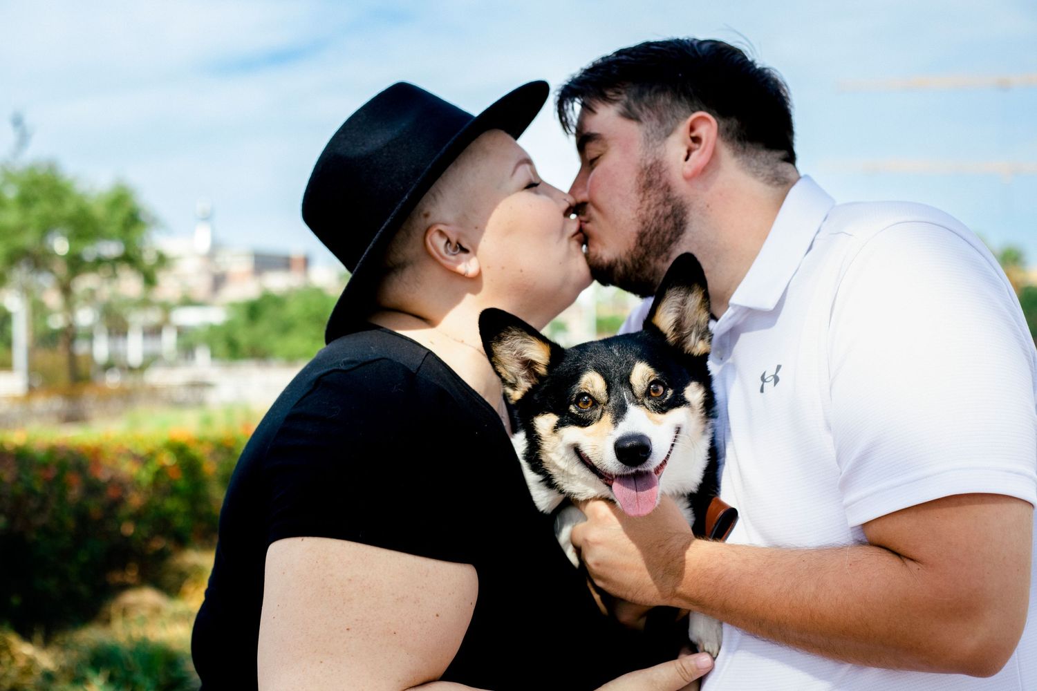 Couple kissing while holding their corgi.