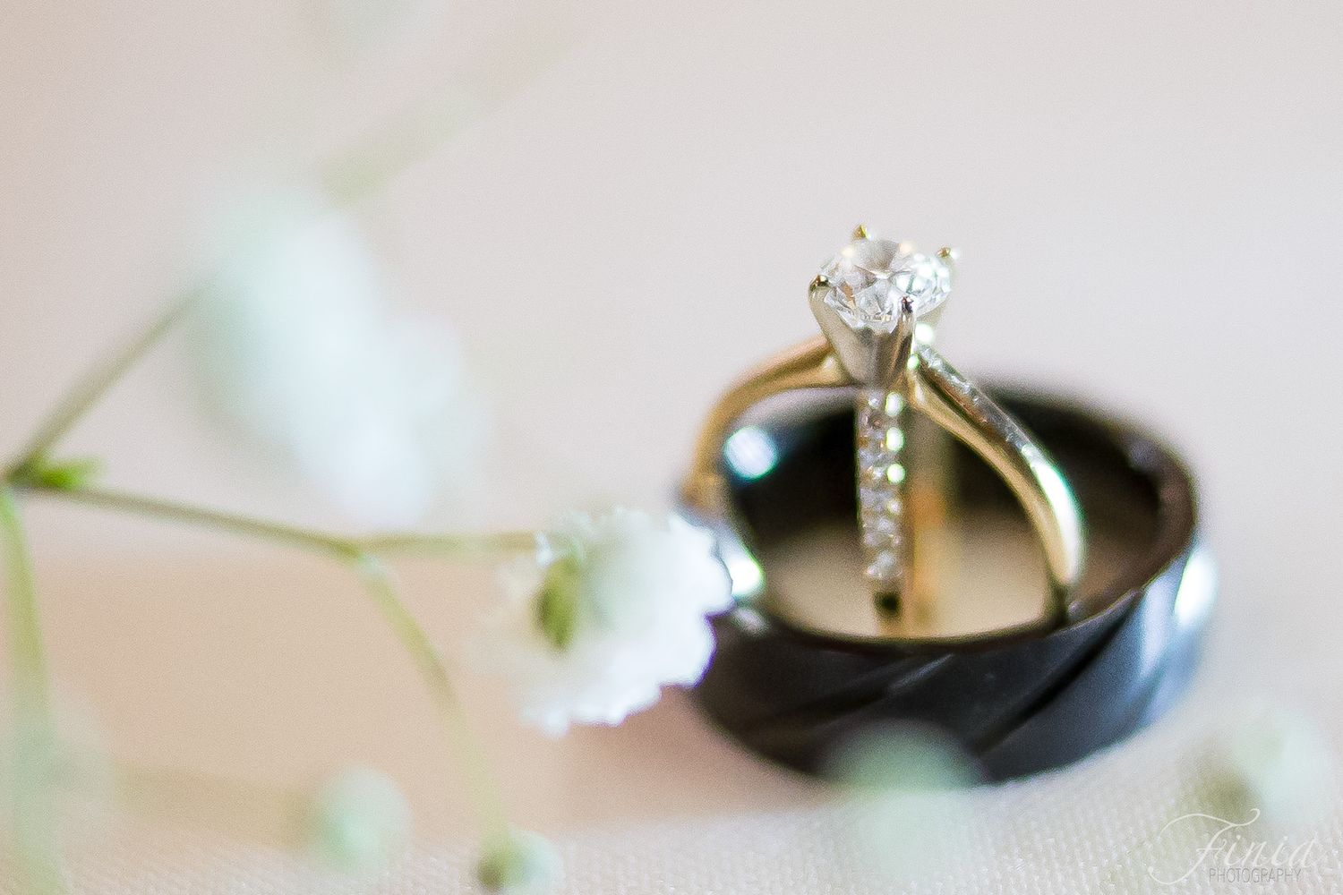 Close-up of wedding rings and diamond engagement ring with delicate white flowers in soft focus.