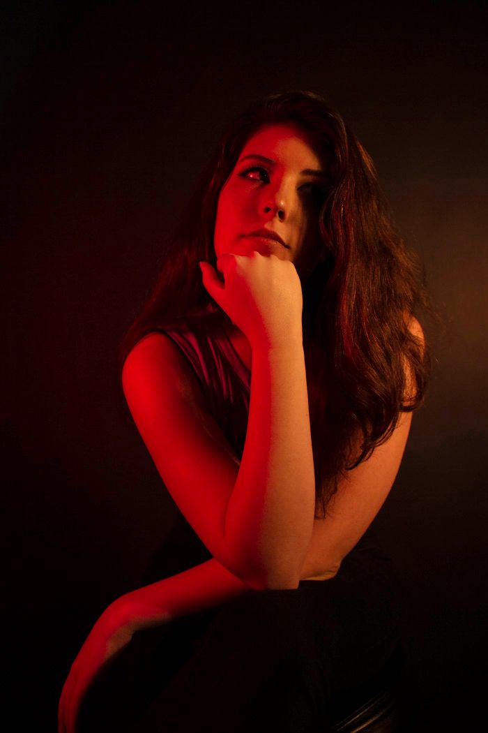 Artistic portrait bathed in deep red lighting against dark background.