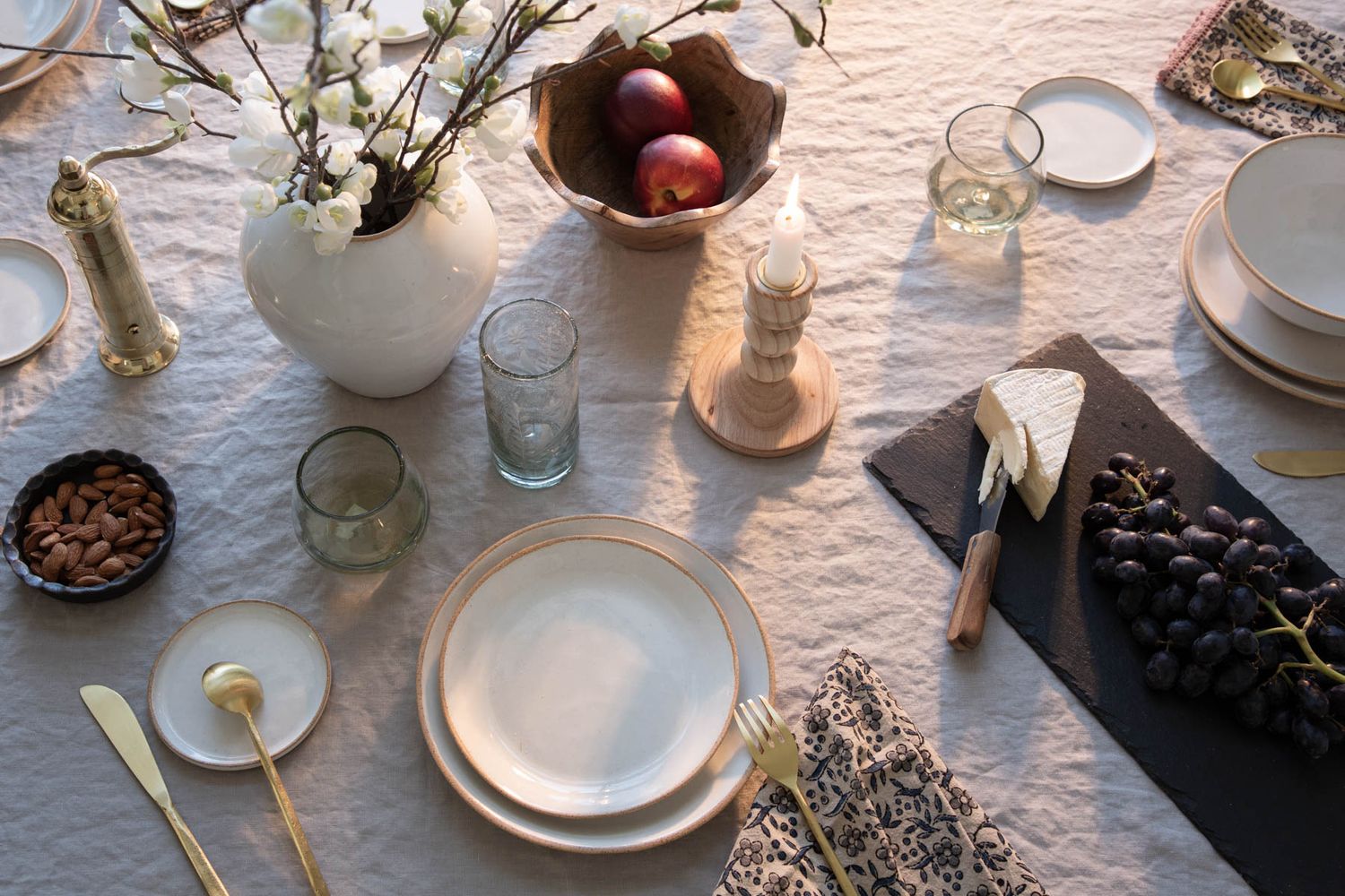 Table setting with white dishes, flowers, and fruit bowl on linen tablecloth.