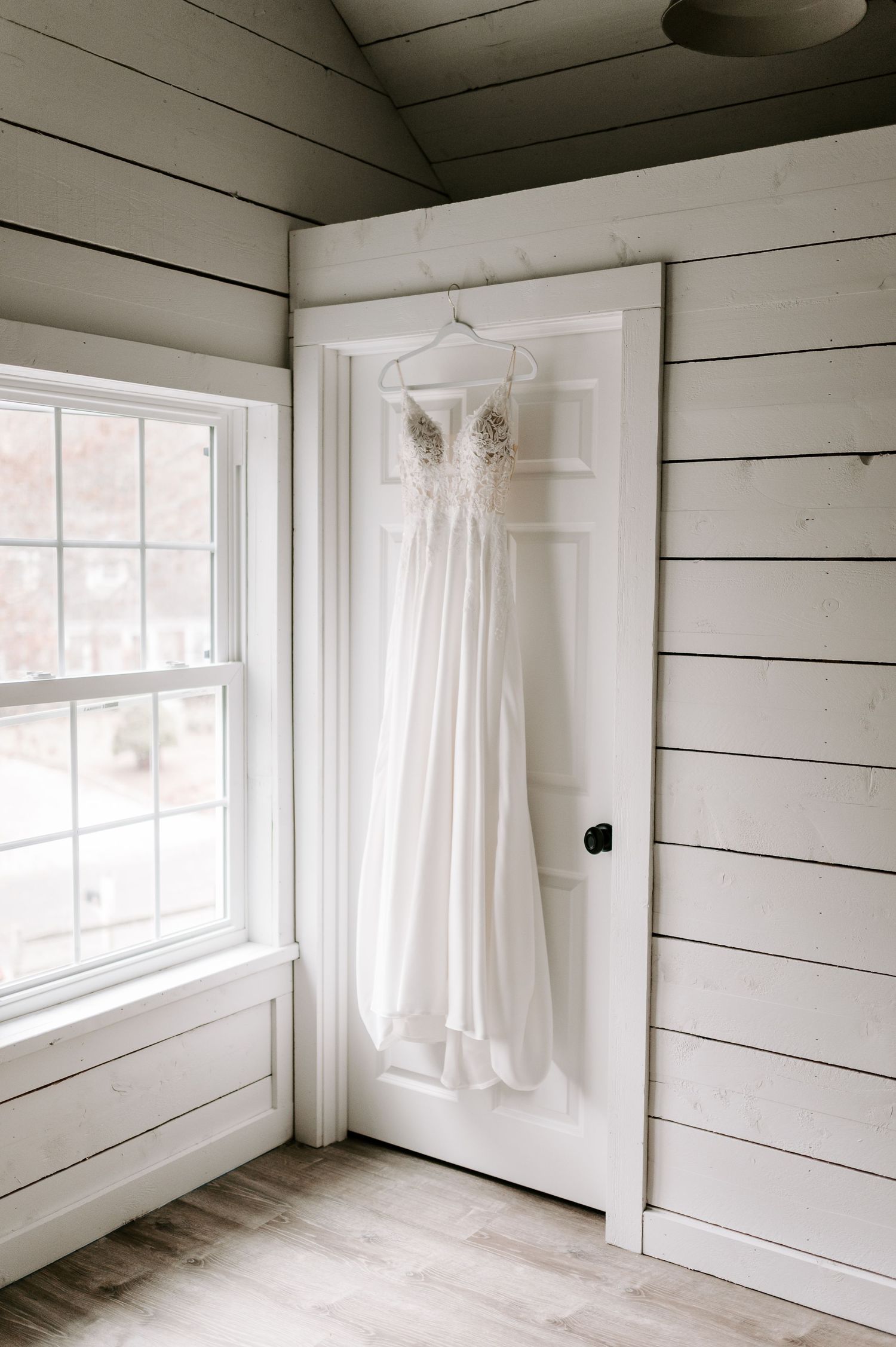 Bright white room with shiplap walls and hanging wedding dress by window.