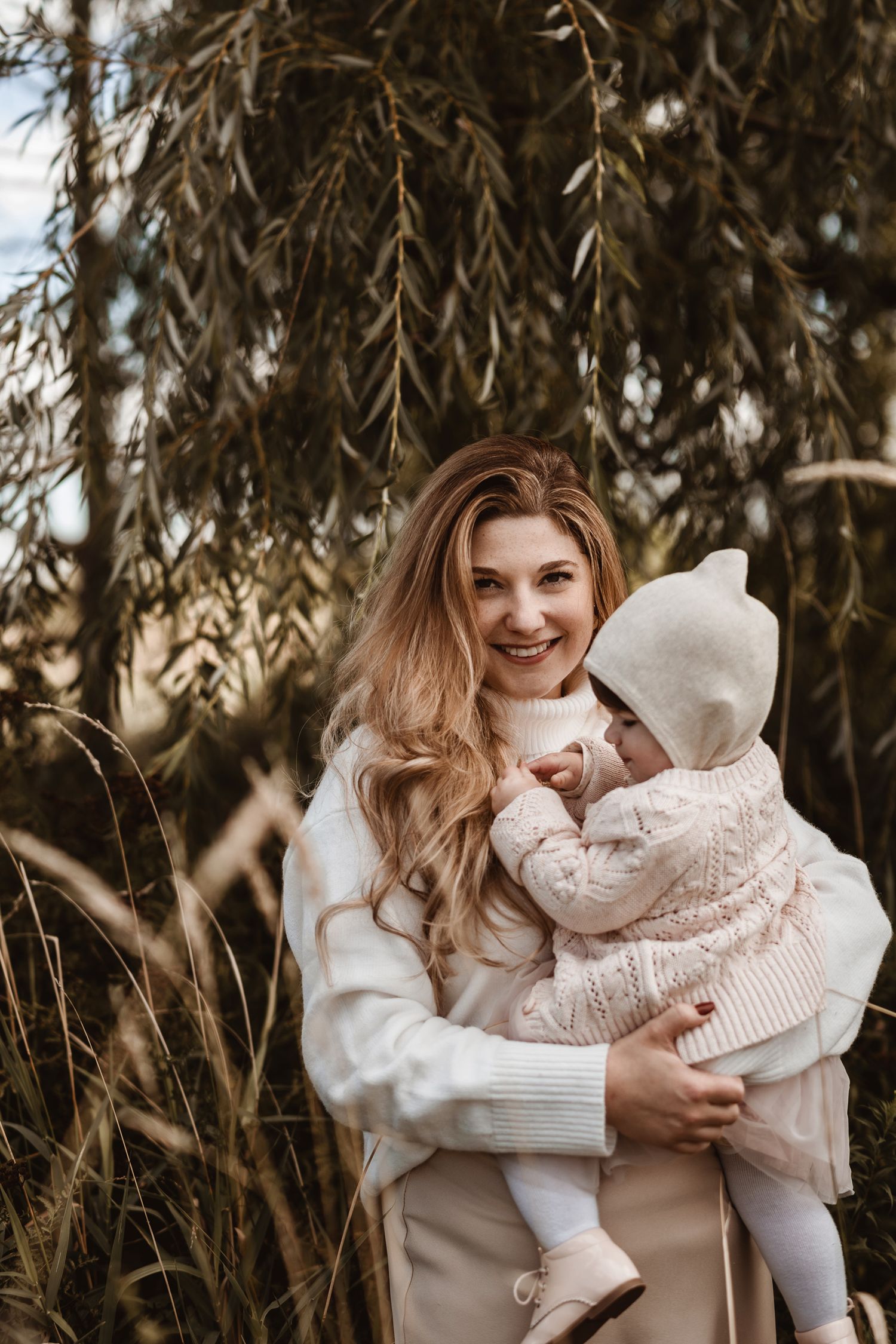 Outdoor family moment captured under drooping willow branches in warm autumn light.