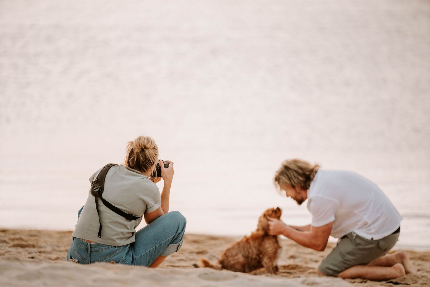 A photographer captures images of a dog on the beach during a photo shoot.