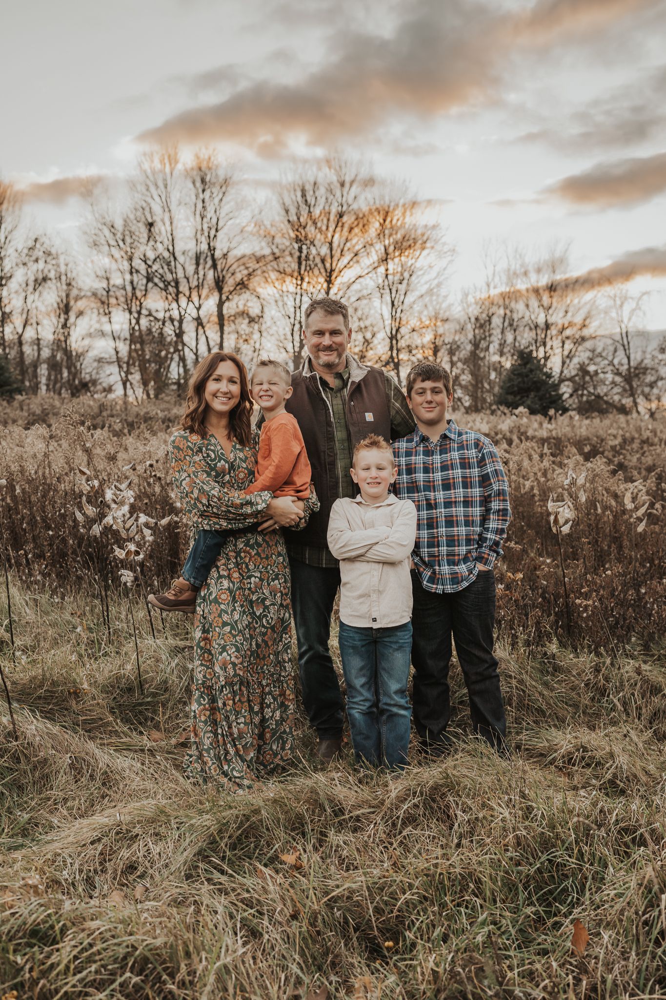Family group stands together in tall grass against a sunset sky with bare trees in background near Hanover Michigan.
