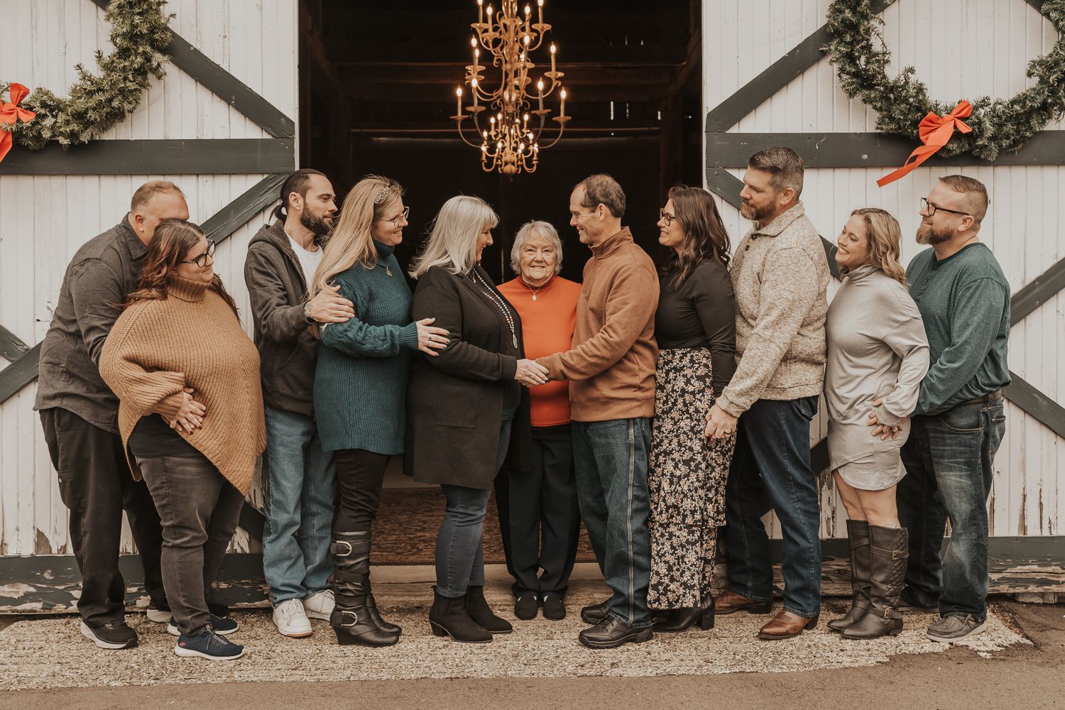Extended family photographed against white barn wall with decorative lighting in Jackson MI.