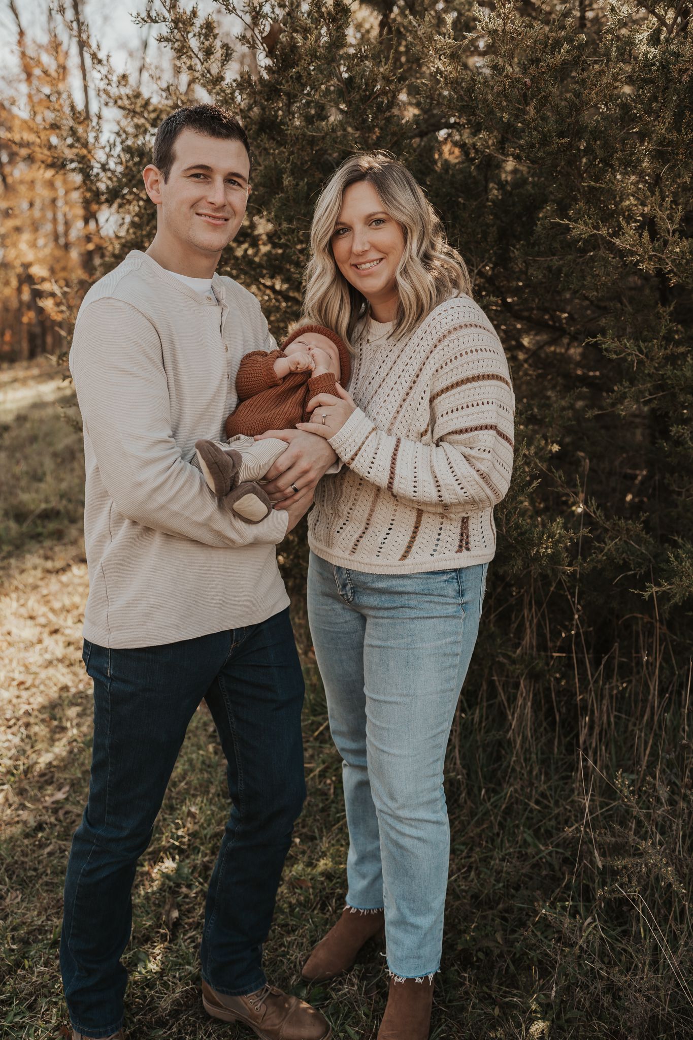 A family shares tender moments while wearing coordinated neutral outfits in an outdoor setting.