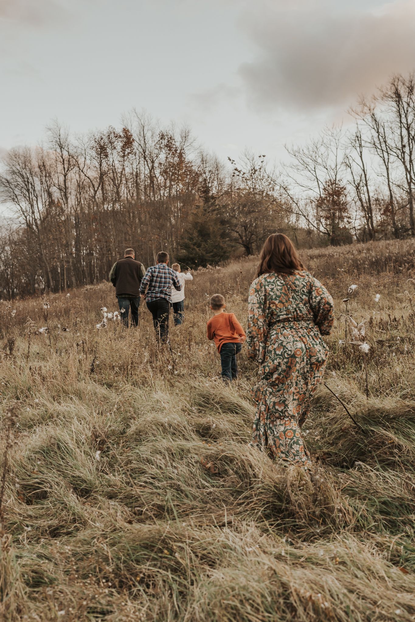 Family walking through a field of tall grass during golden hour with trees in background.