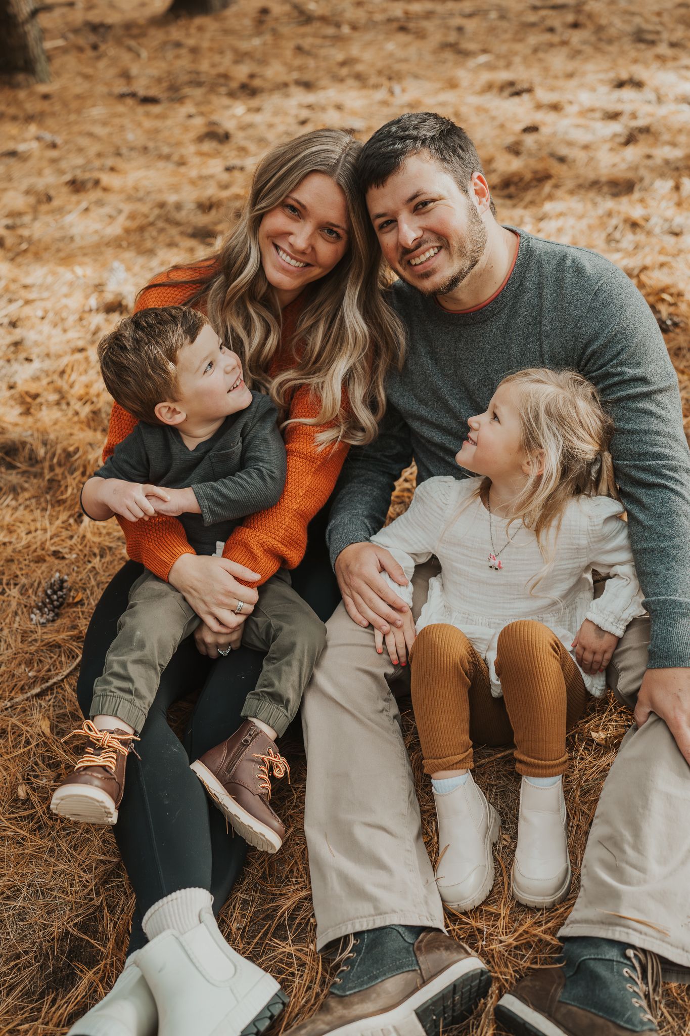A casual family portrait with everyone sitting and smiling on forest ground.