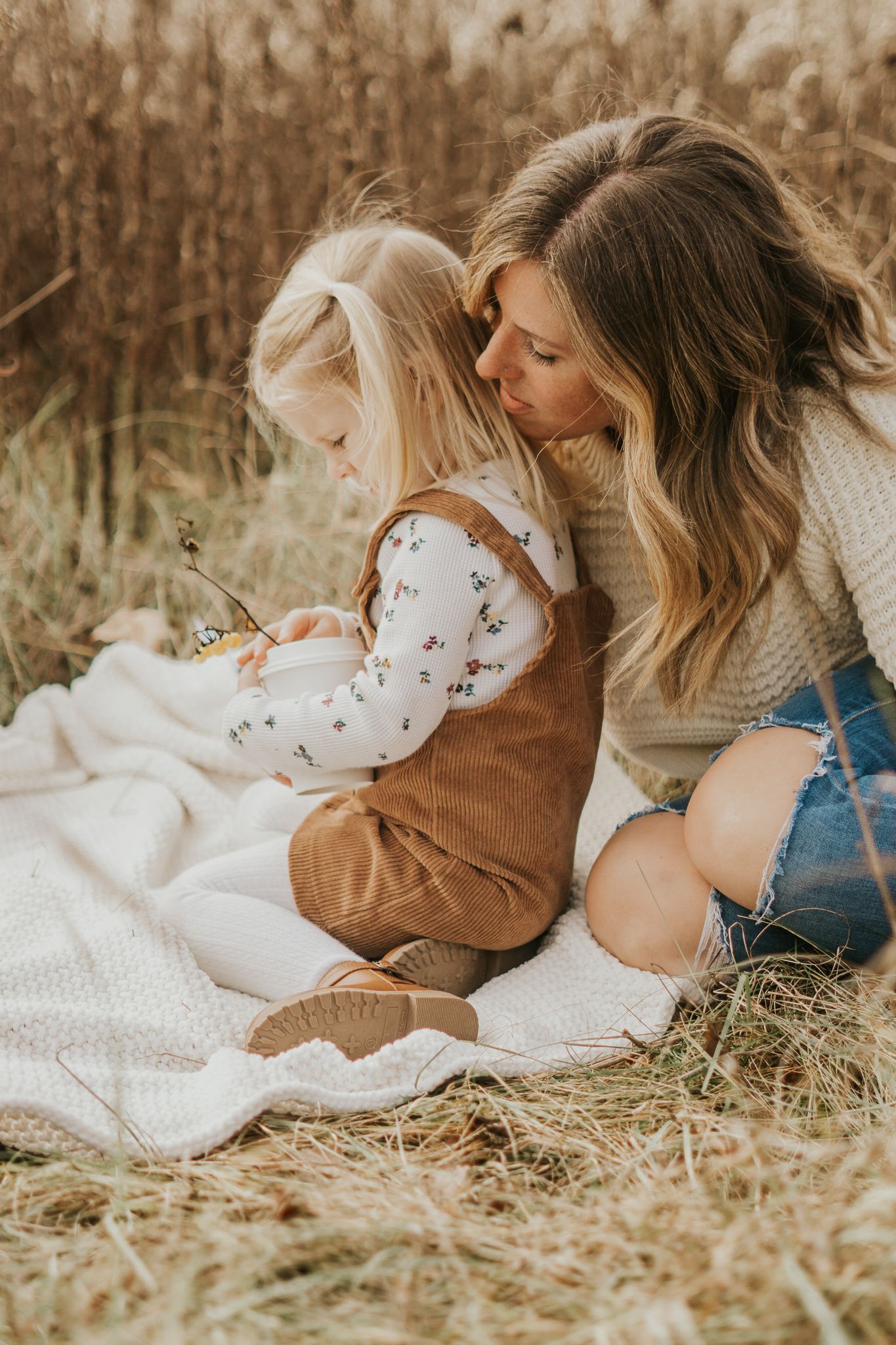 Intimate family moment captured on a blanket in a rustic field setting.