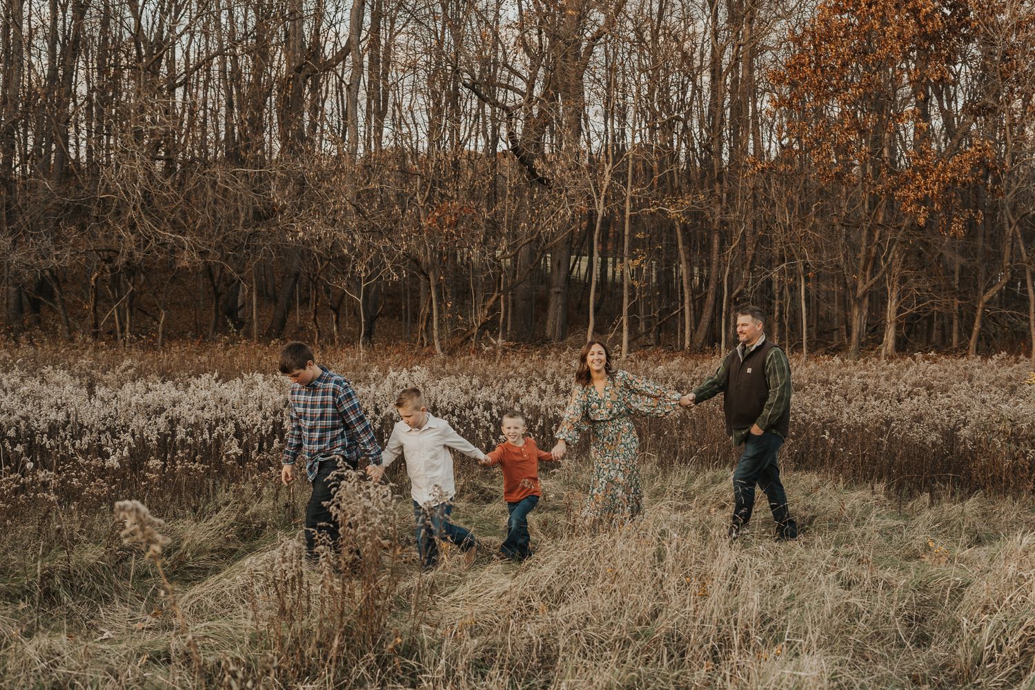 Family members walk and play together through tall grass in an autumn field at sunset.