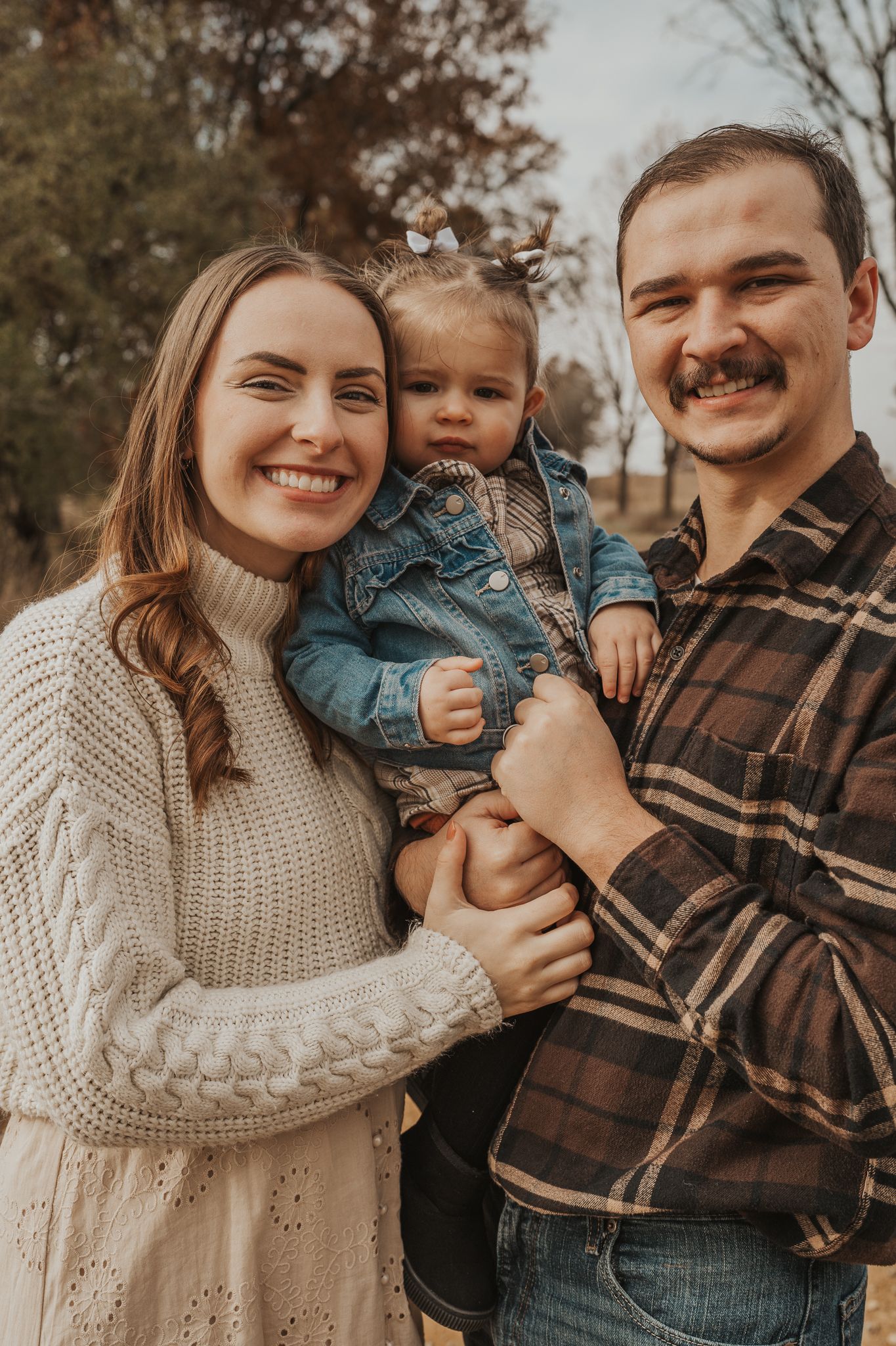 A cheerful family portrait taken outdoors with autumn colors in the background.