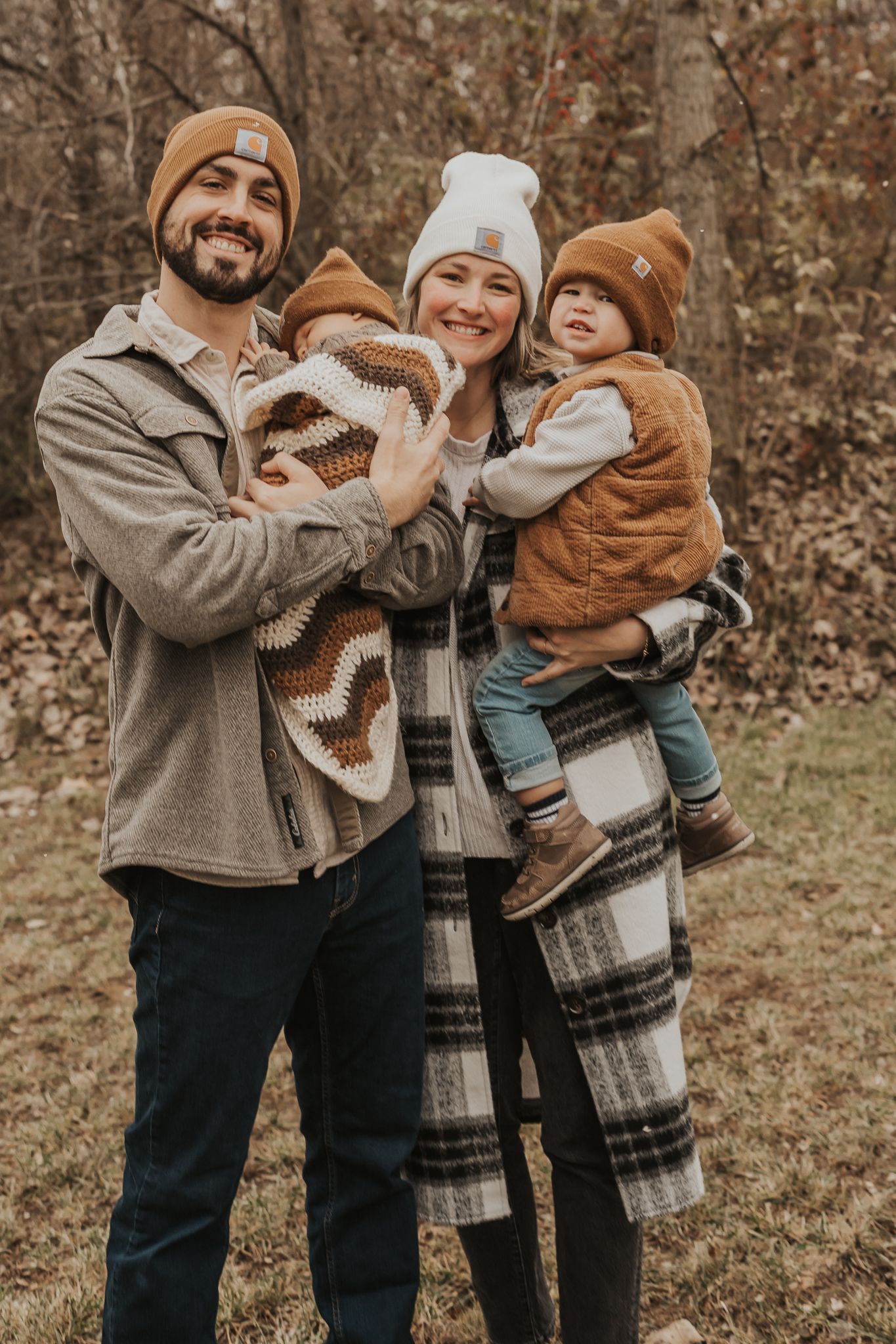 Candid newborn photograph of family moment in coordinated winter outfits and plaid blanket.