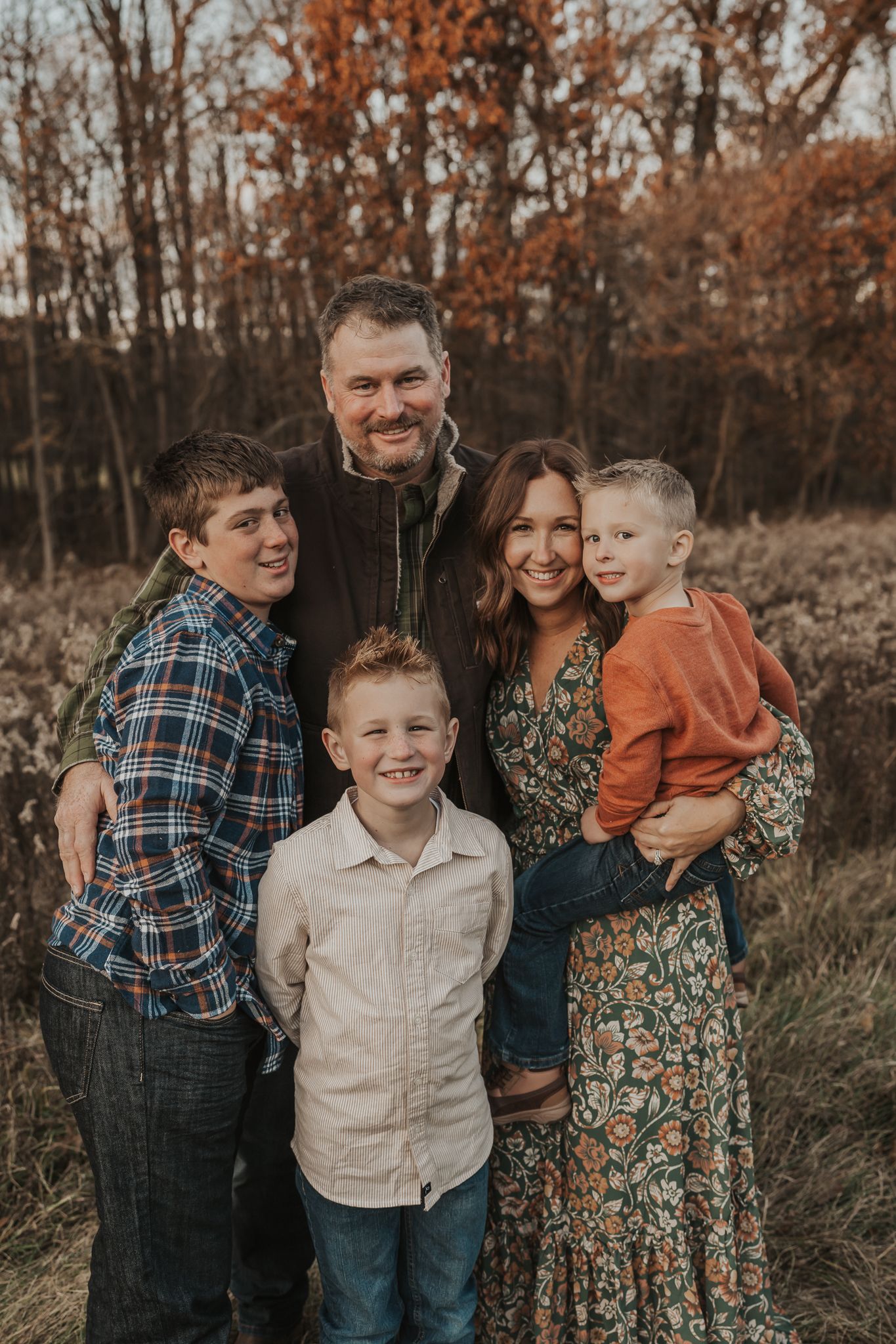 Casual family portrait session captured in a field with autumn colors and natural lighting.