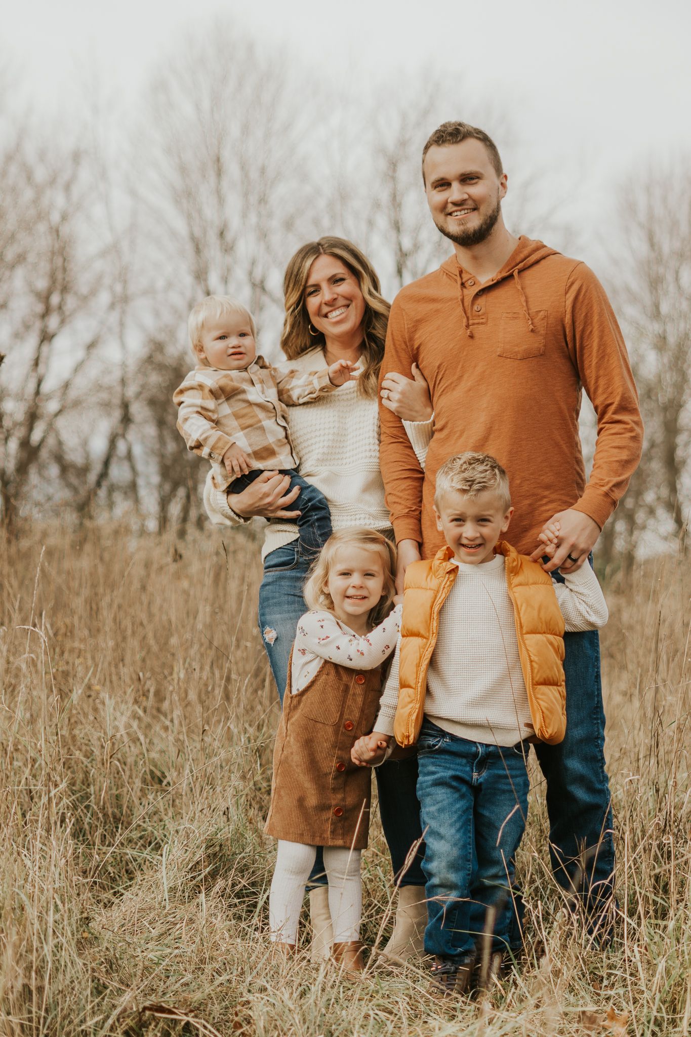 Family portrait in a rustic field wearing coordinated autumn-colored clothing.
