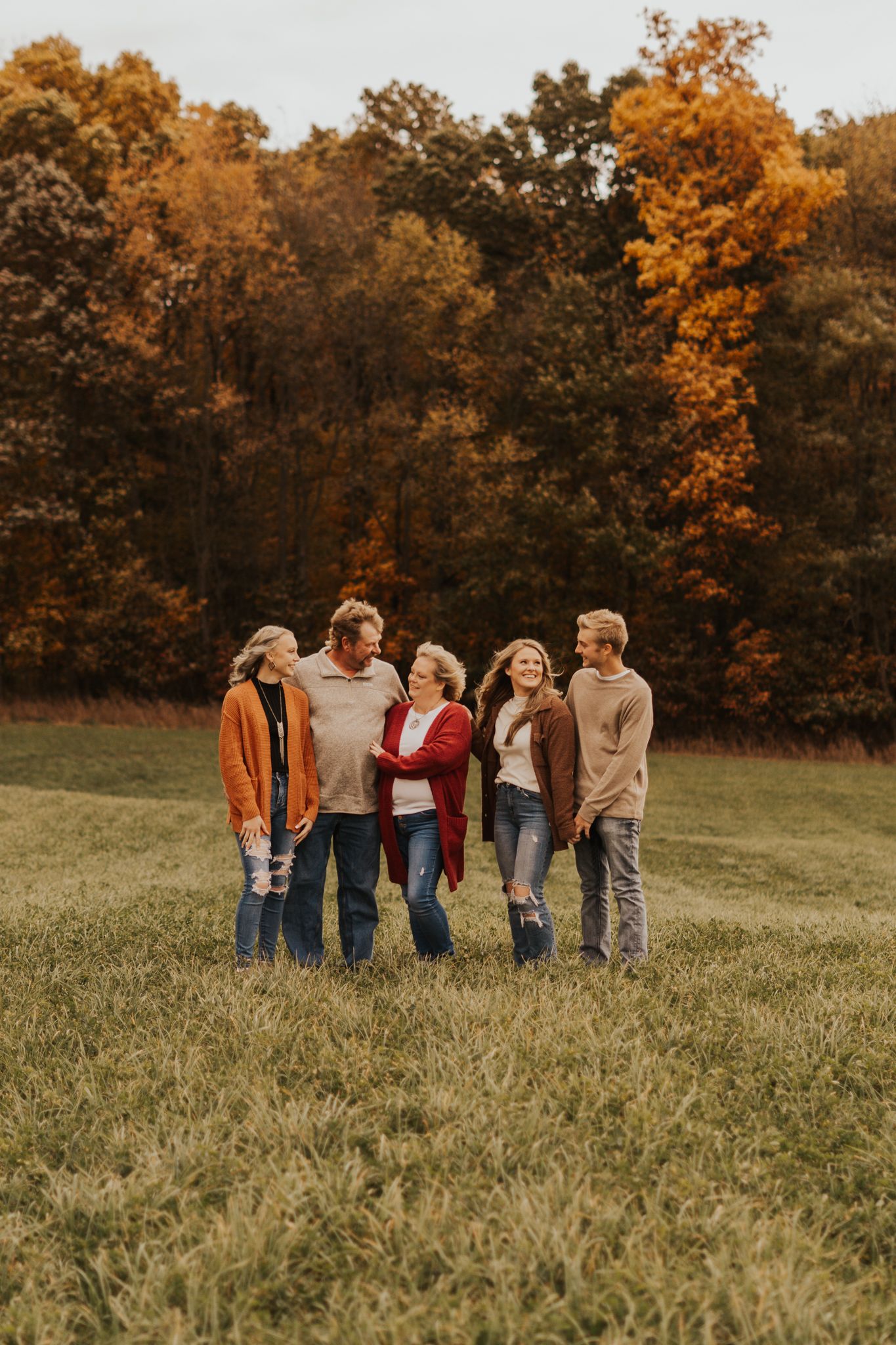 Group of people gathered in a grassy field during autumn with colorful trees in the background.