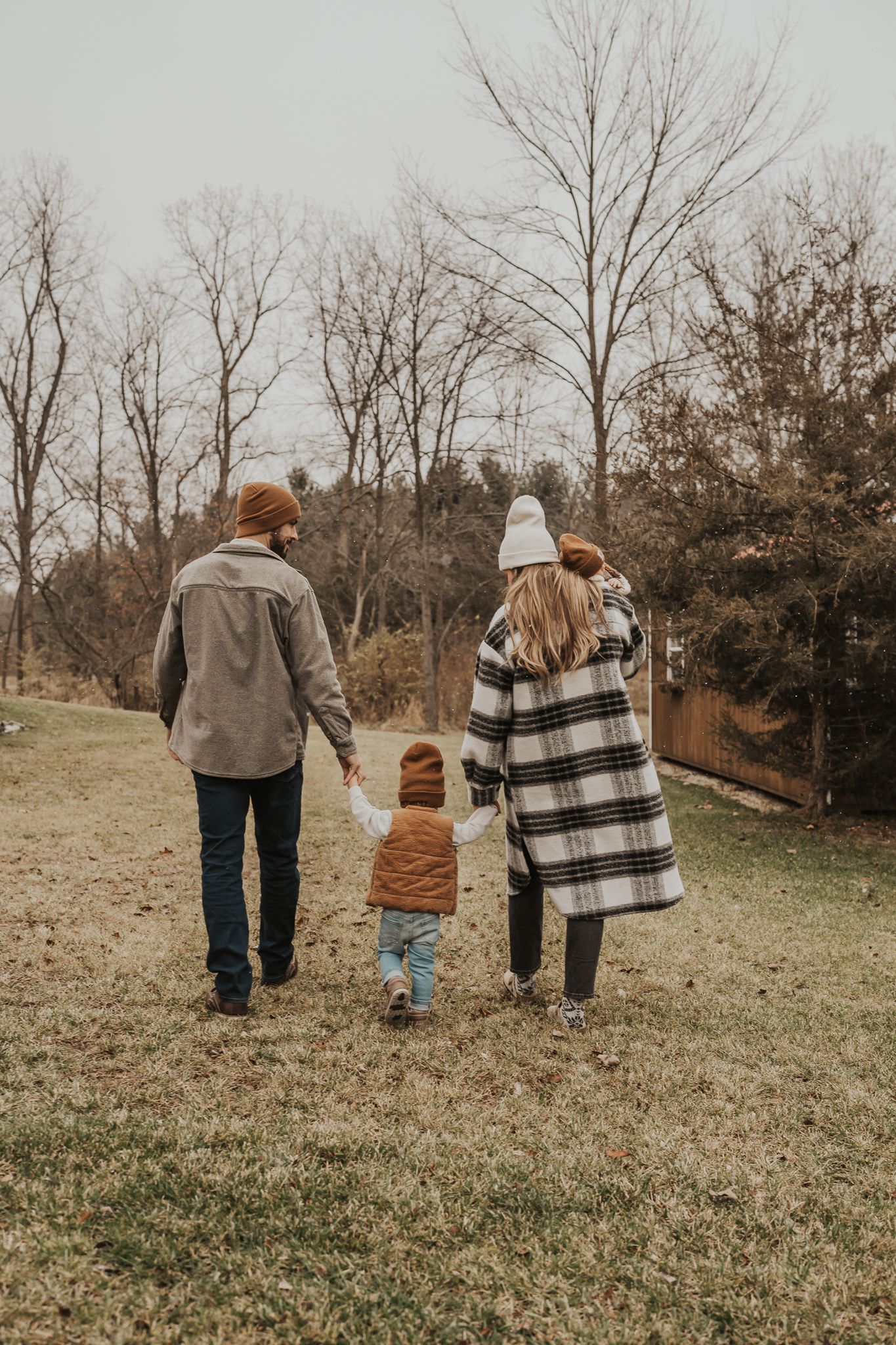 Family walking away from camera on grassy hill during autumn day.
