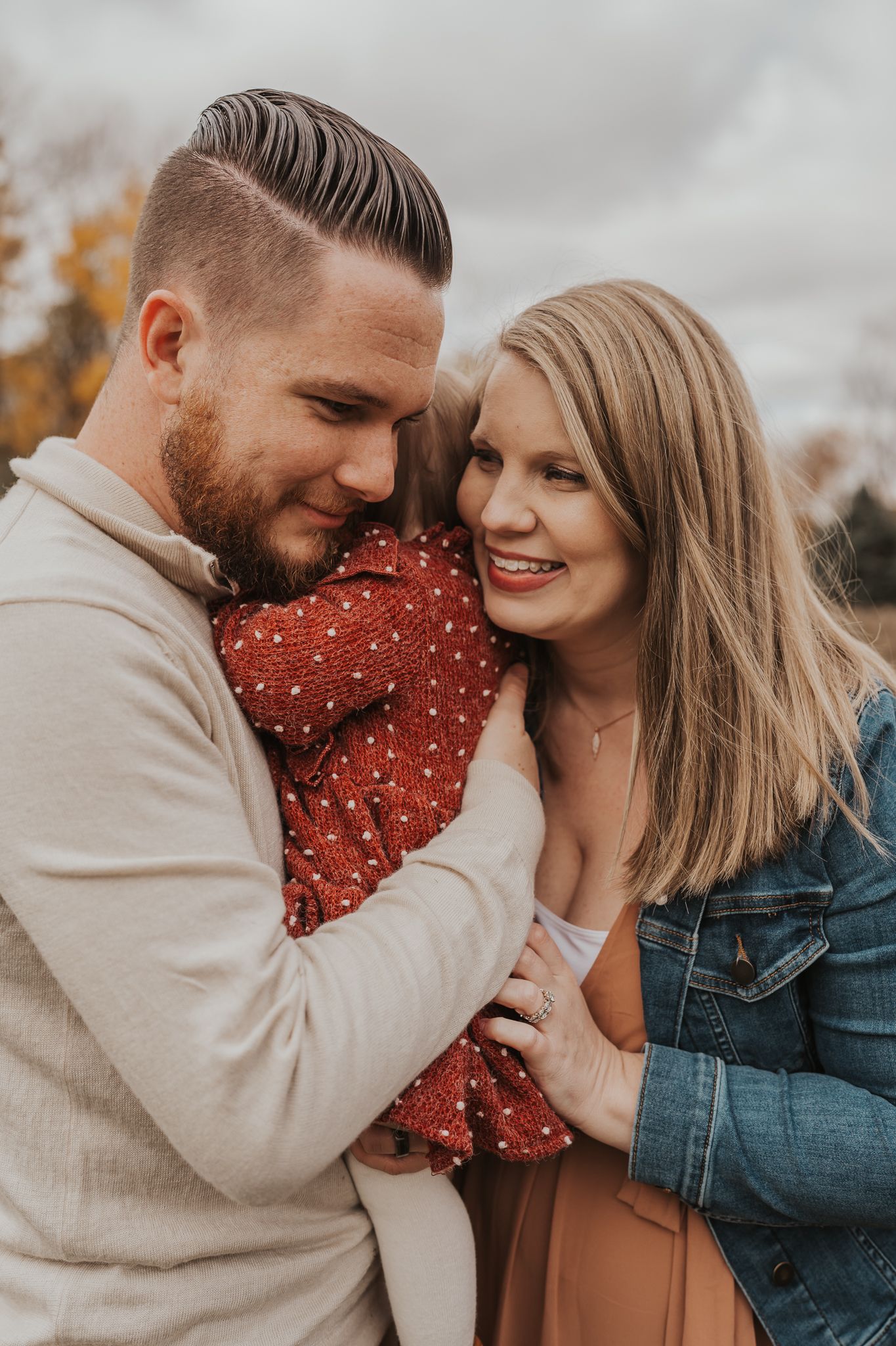 A tender family moment captured in warm autumn tones with fall foliage in the background.