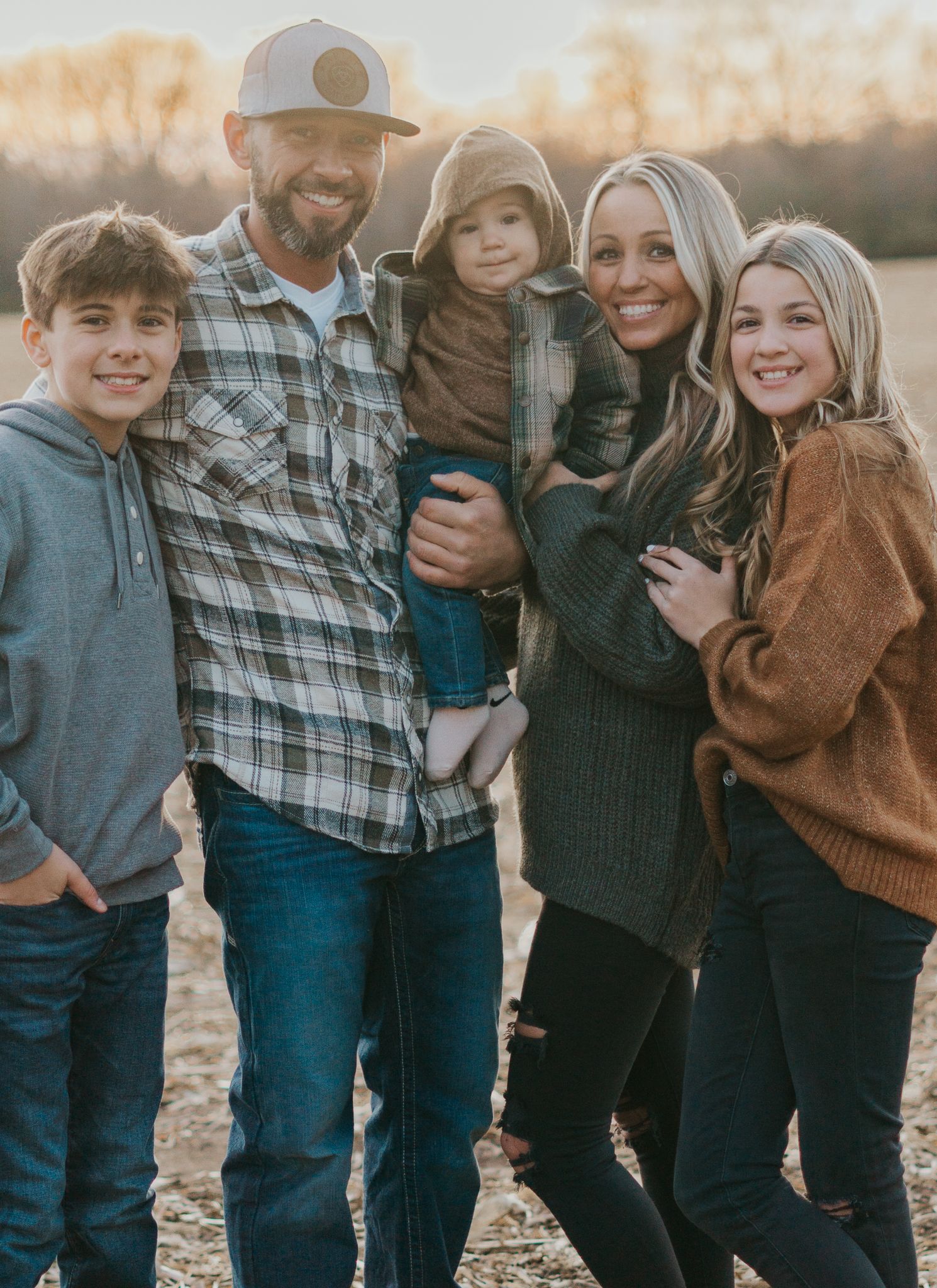 Family members wearing casual attire stand together against a warm autumn backdrop.