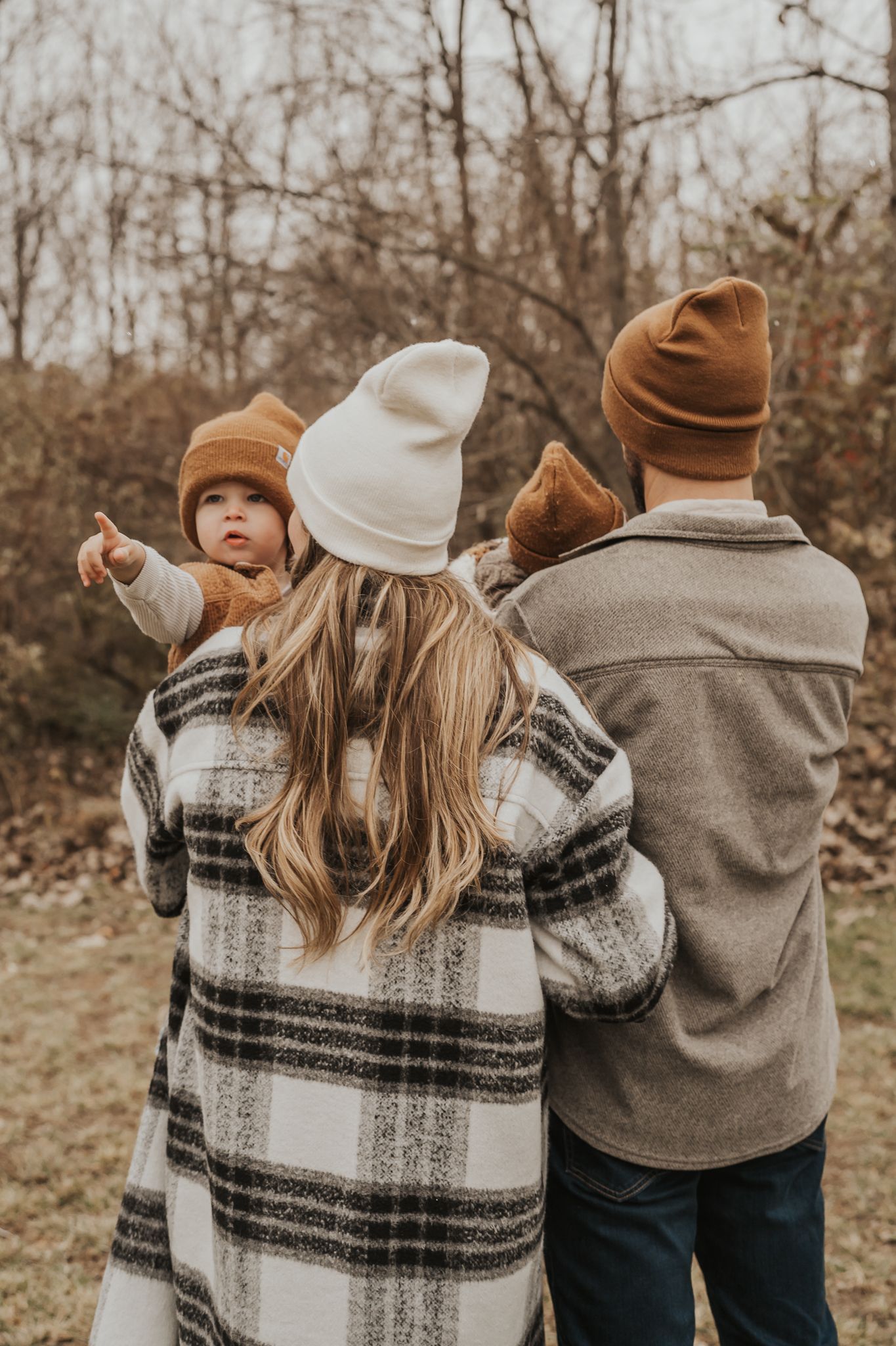 Family wearing winter hats and plaid blanket standing together outdoors.