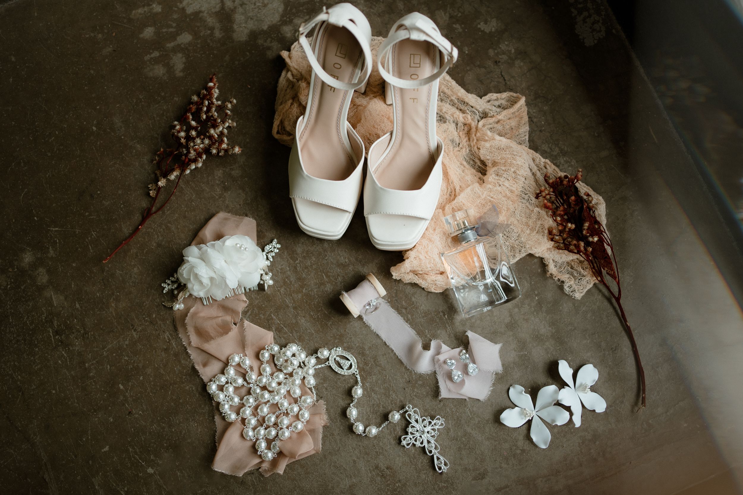 Wedding accessories including white shoes and delicate floral decorations arranged on dark background.