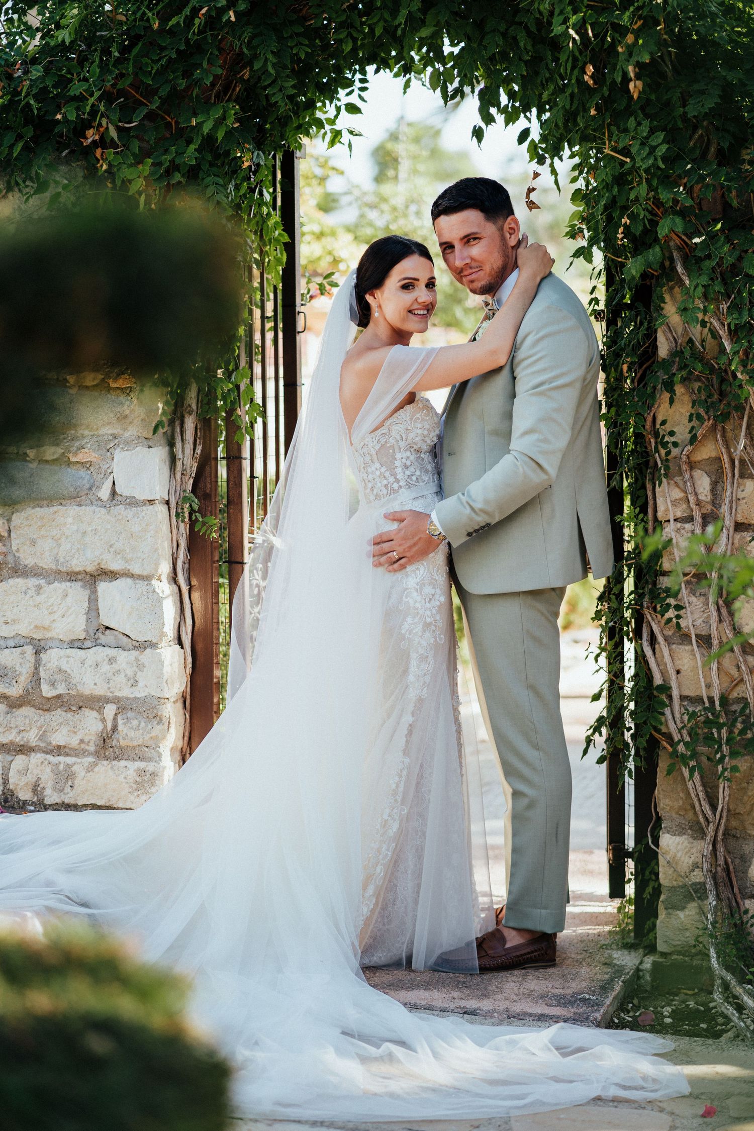 A romantic wedding portrait under a vine-covered archway with trailing greenery.