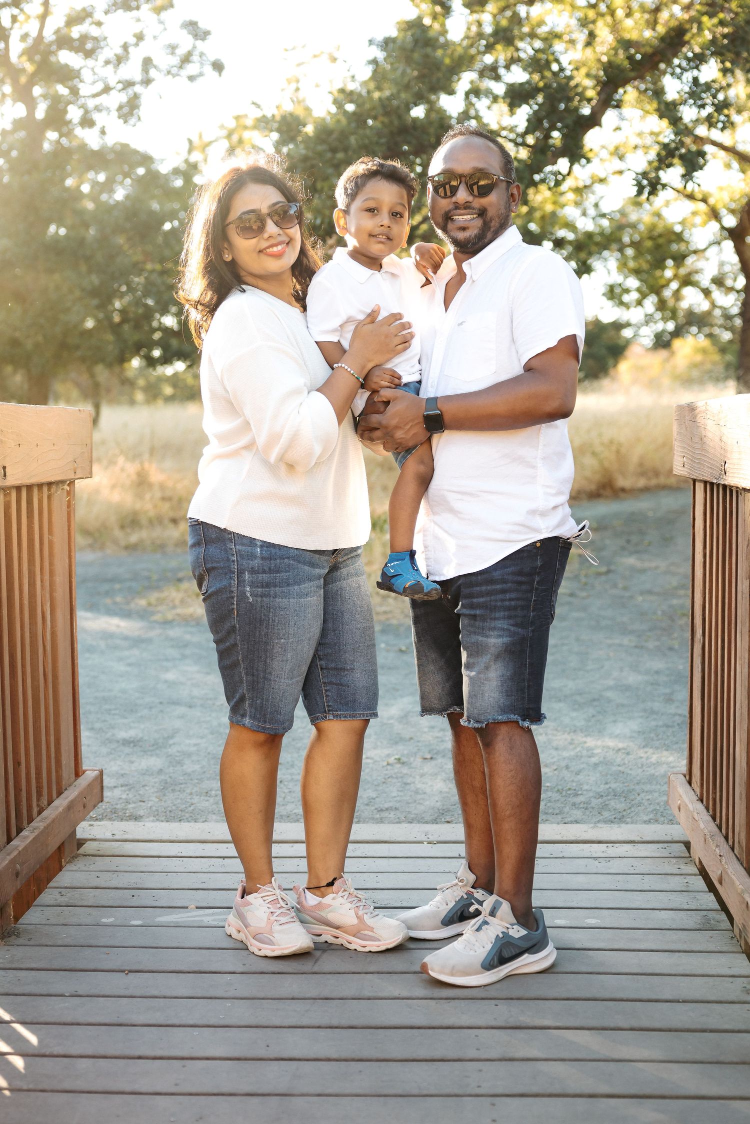 Family standing on wooden bridge during golden hour sunset.