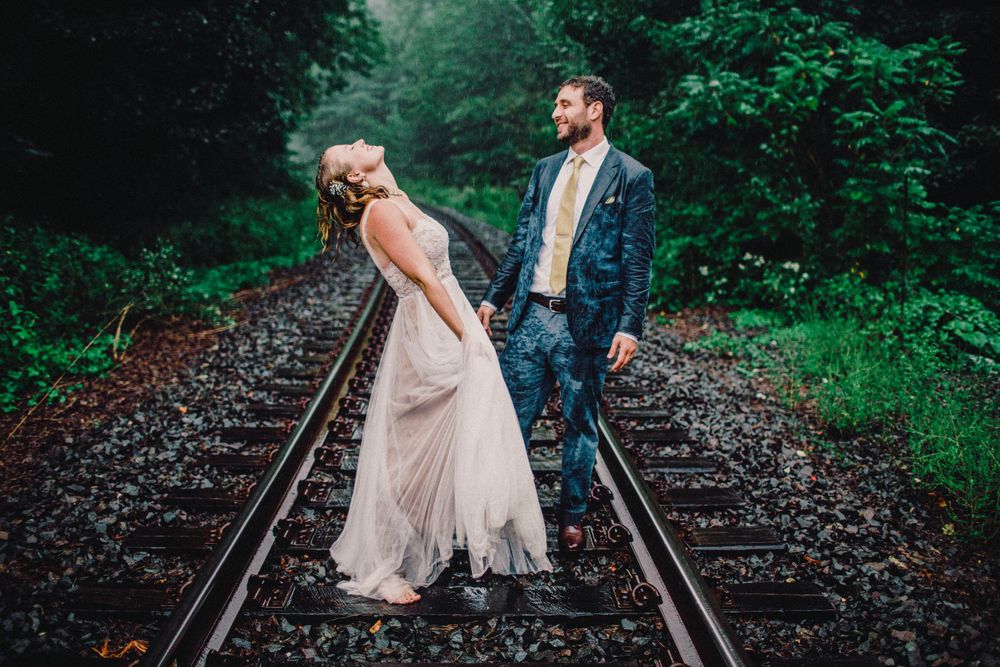 Romantic couple posing on train tracks in a lush green forest setting.