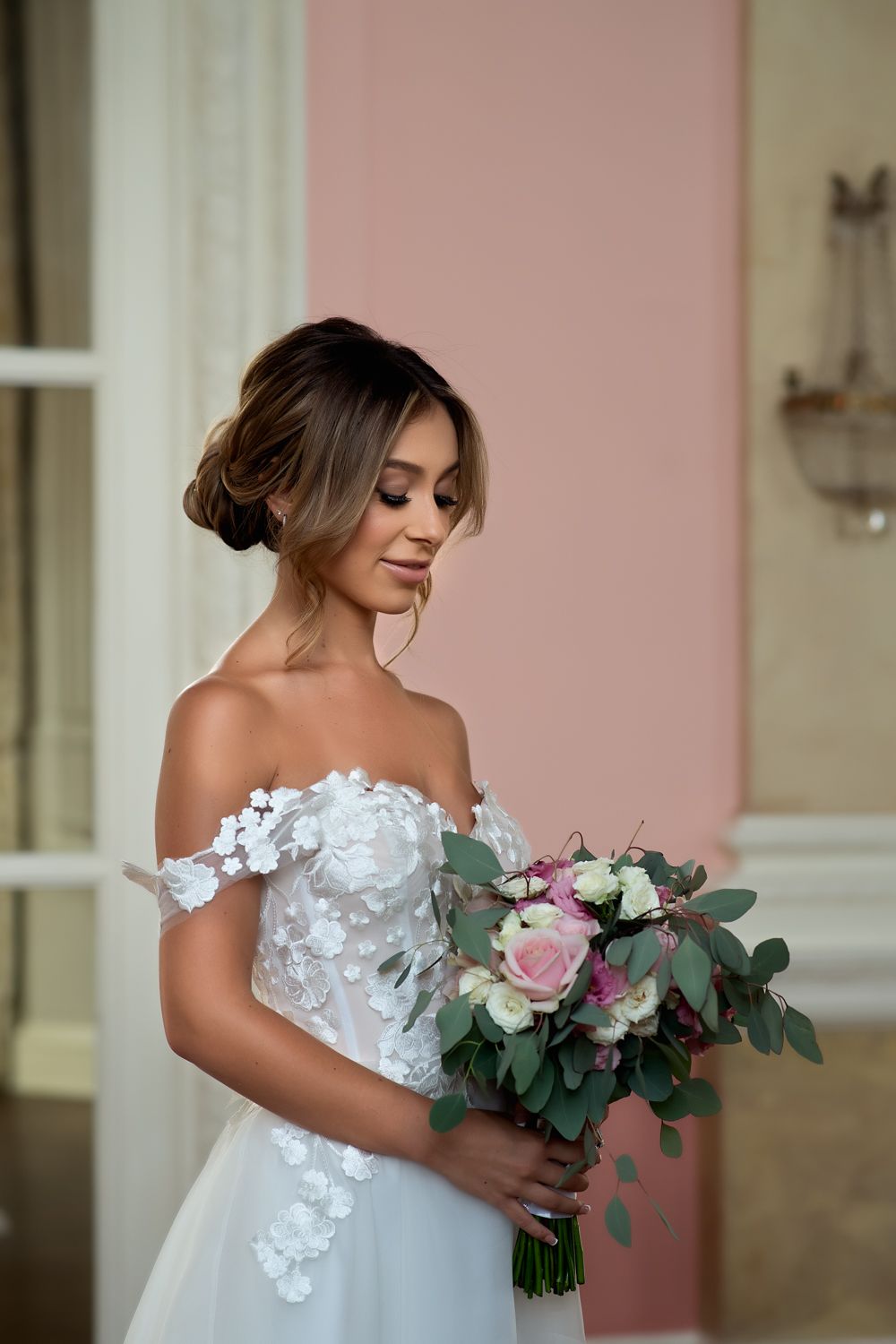 A delicate bridal portrait with off-shoulder lace dress and pink floral bouquet.