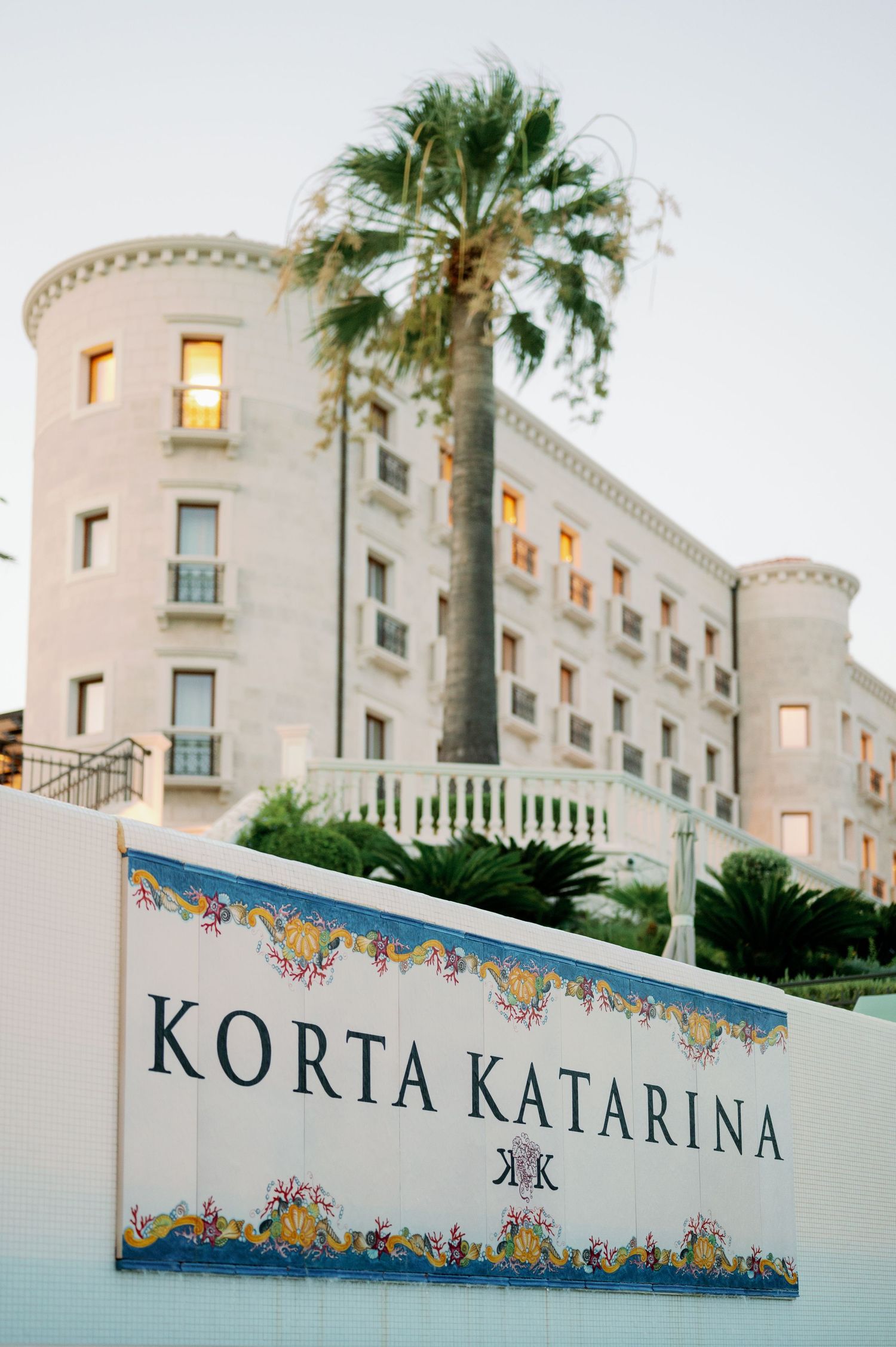 The Korta Katarina hotel exterior with palm trees and decorative sign at twilight.