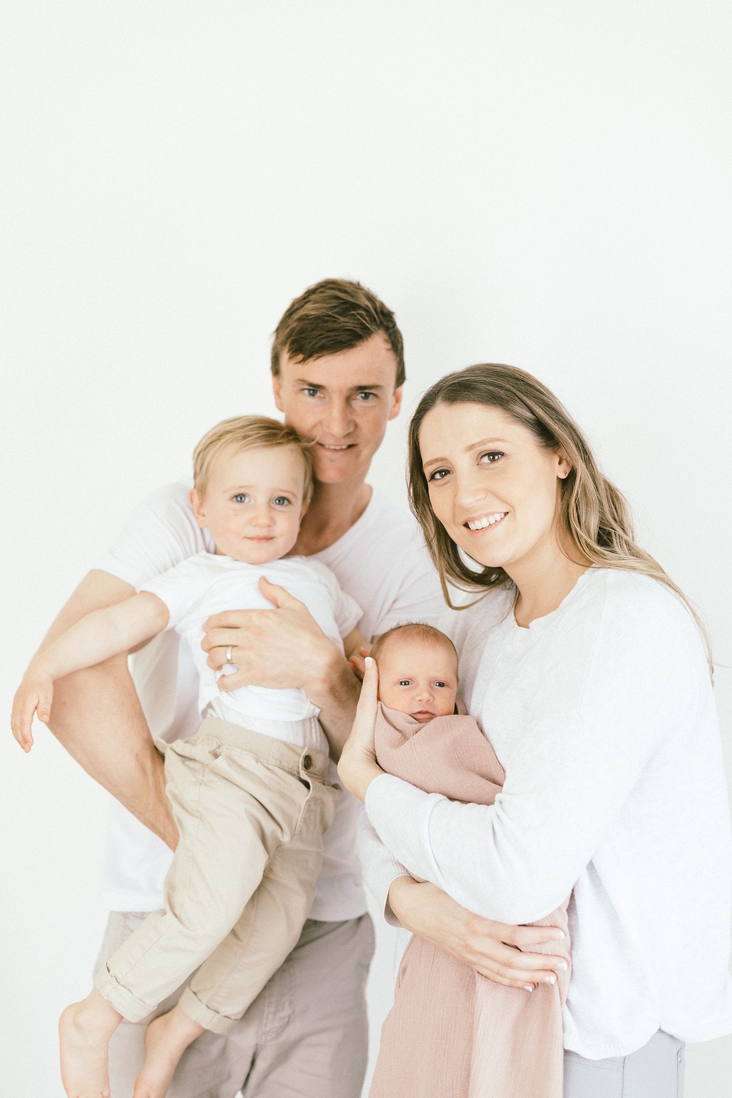 Modern family portrait with parents and two children against white background.