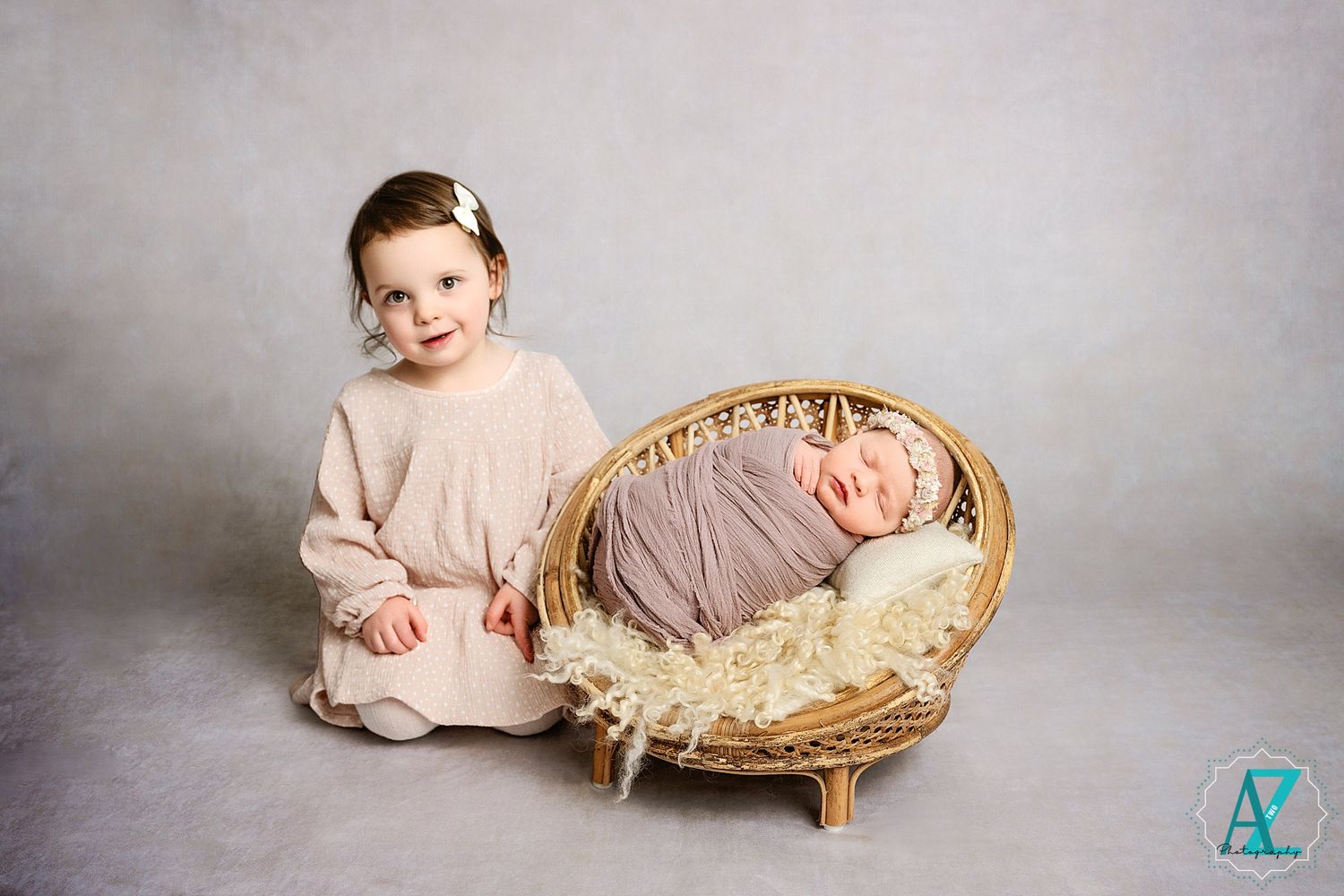 Sibling portrait with wicker basket against neutral grey backdrop.